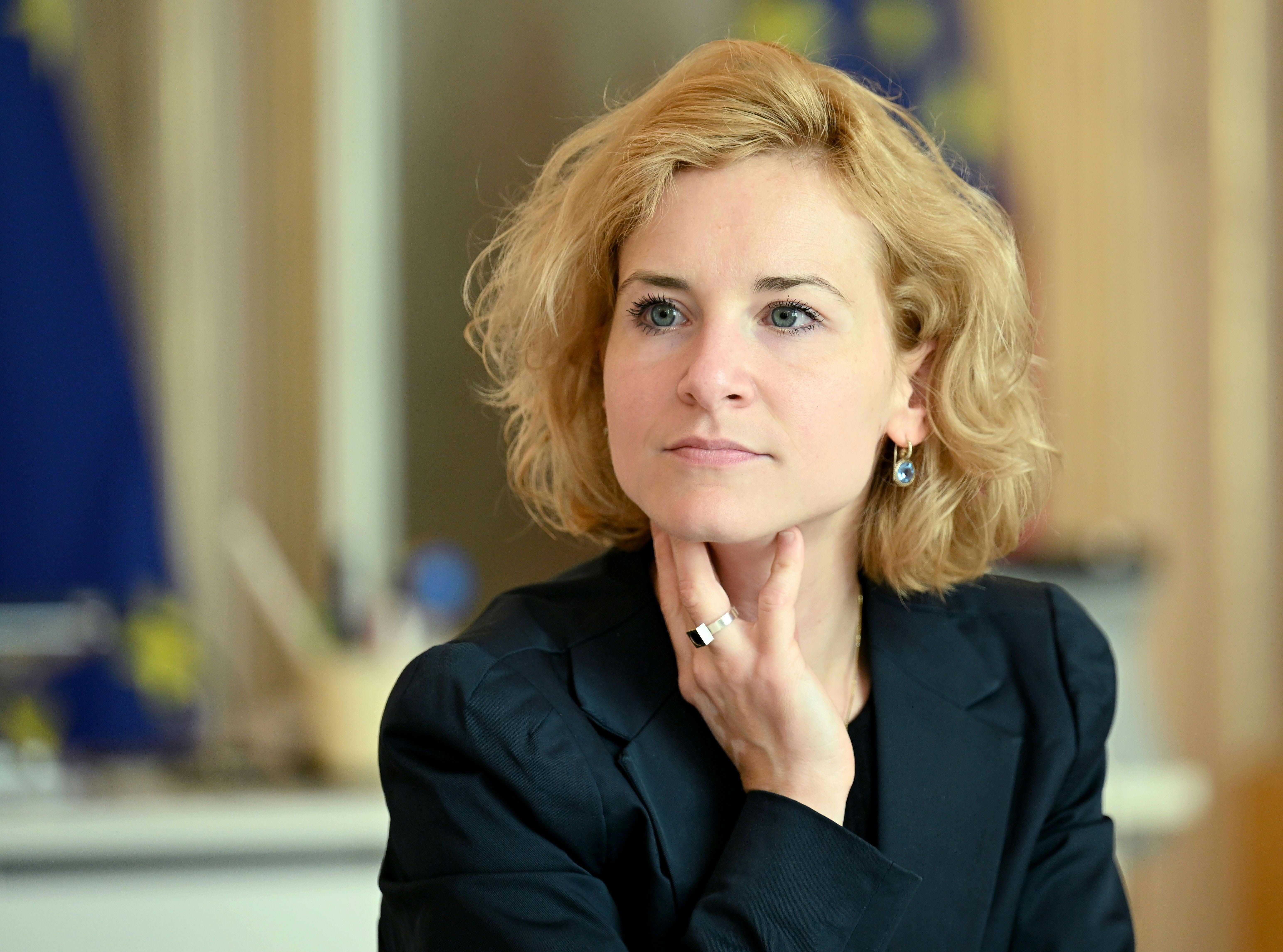 Frau mit blondem, lockigem Haar im dunklen Blazer sitzt gedankenvoll in einem Büro.