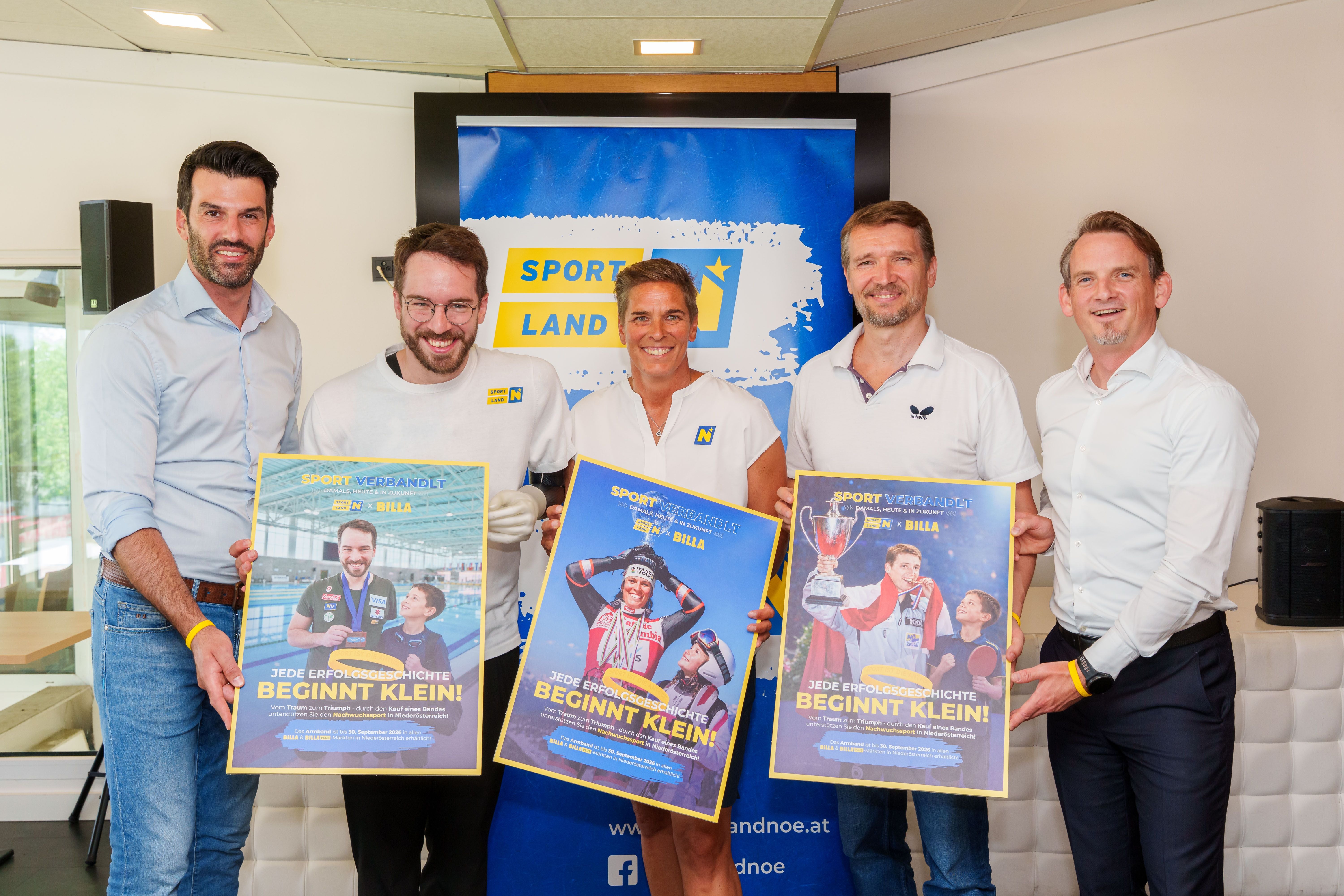 Fünf Personen halten Plakate bei einer Sport-Veranstaltung vor einem "Sportland" Banner.