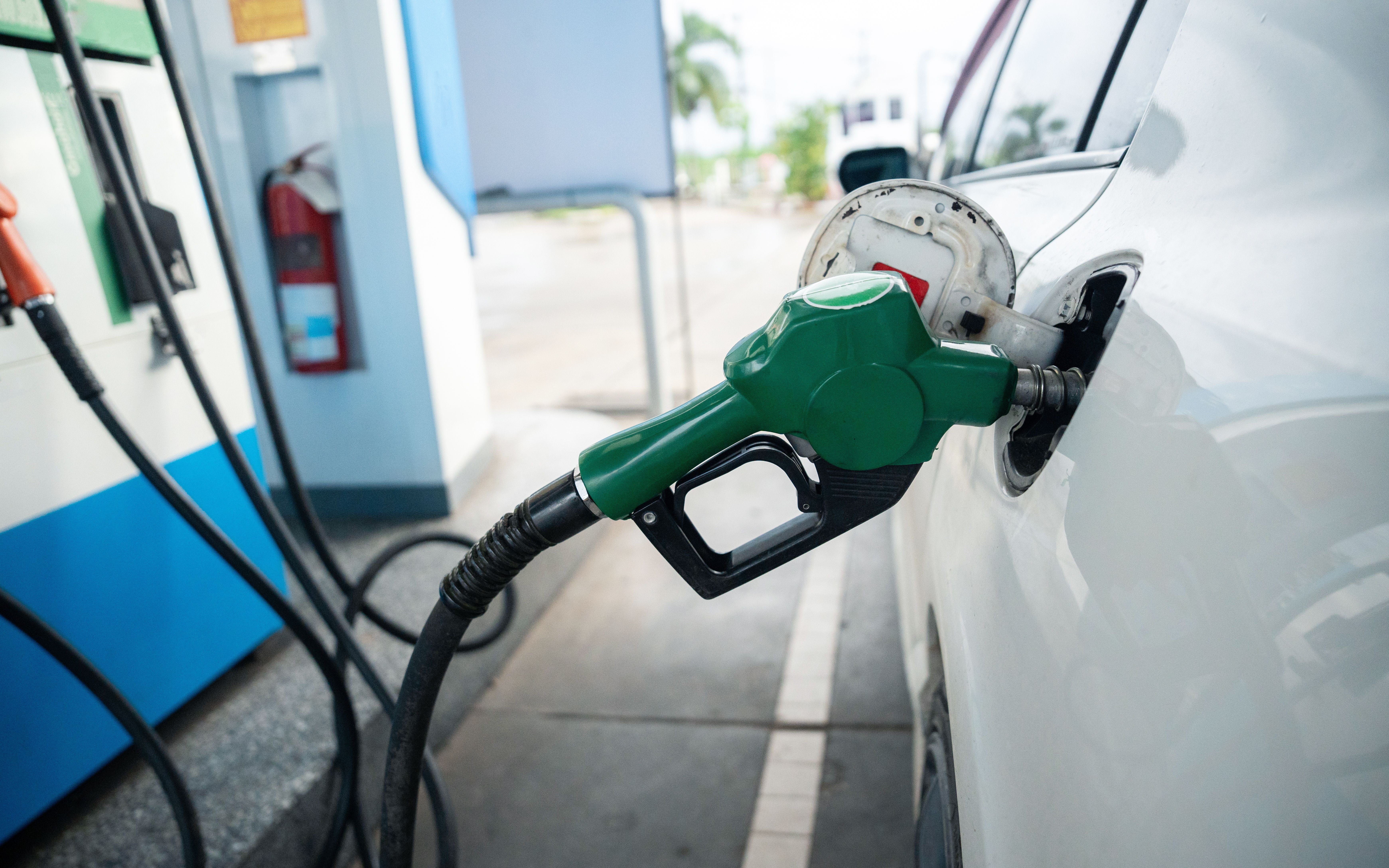 Zapfpistole tankt ein weißes Auto an einer Tankstelle mit grünem Kraftstoffventil.