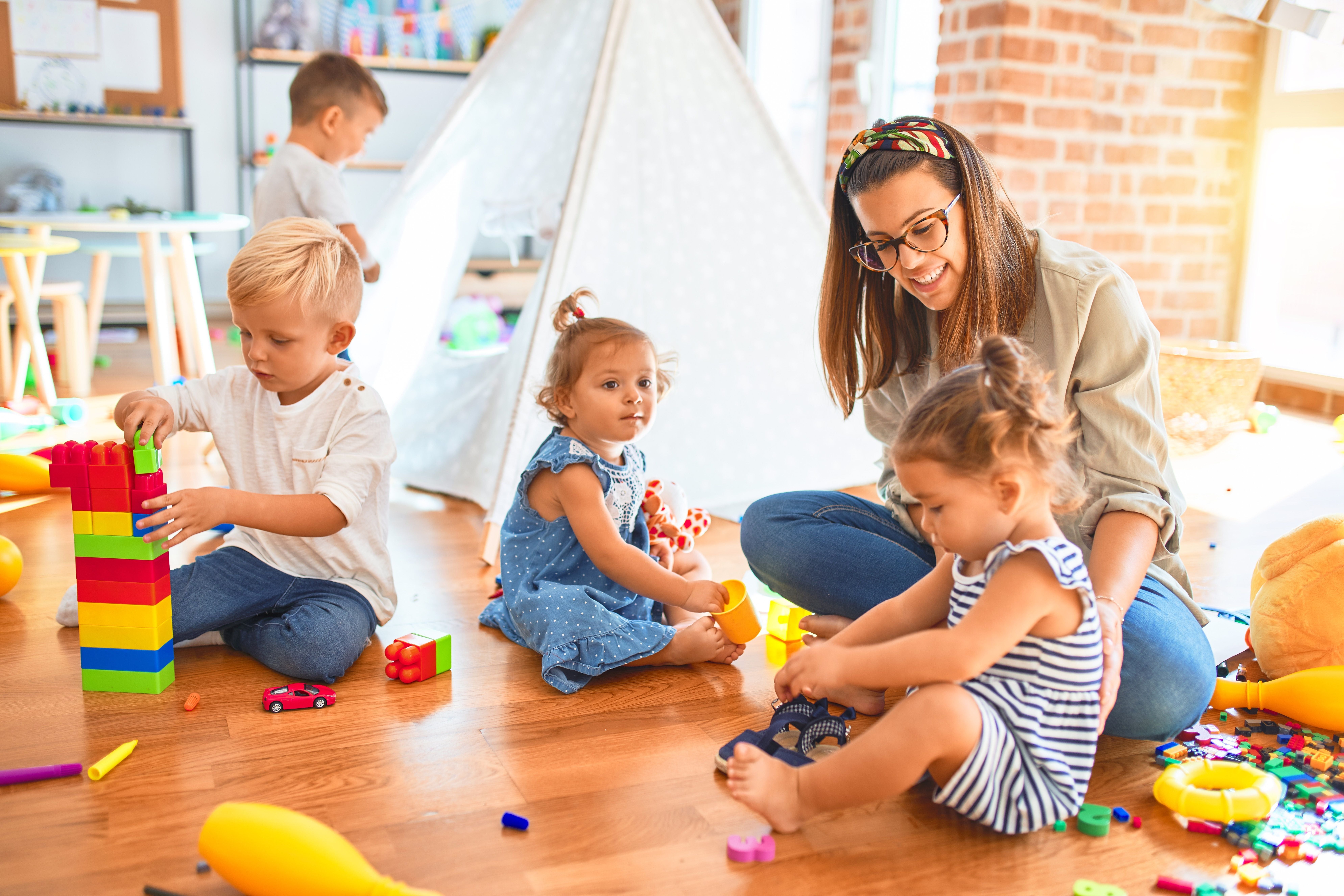 Erzieherin und Kleinkinder spielen gemeinsam mit buntem Spielzeug im Kindergarten.