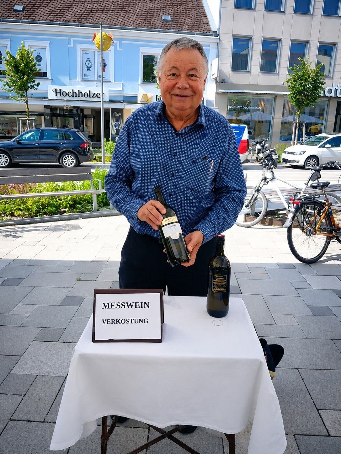 Ein Mann bietet auf der Straße an einem Tisch Wein zur Messweinverkostung an.