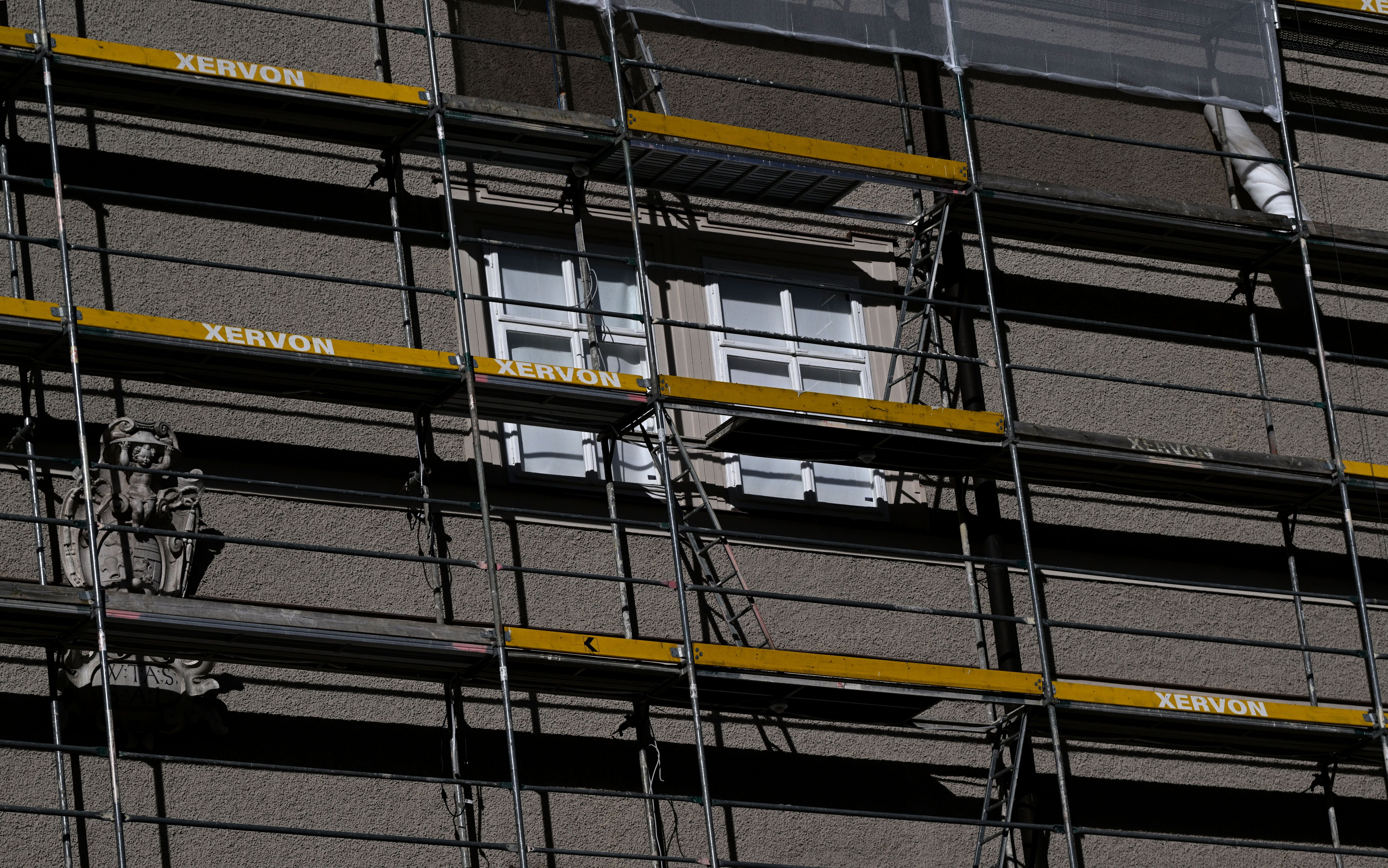 Eingerüstete Hausfassade mit Fenstern und einem Wappenrelief in Salzburg.