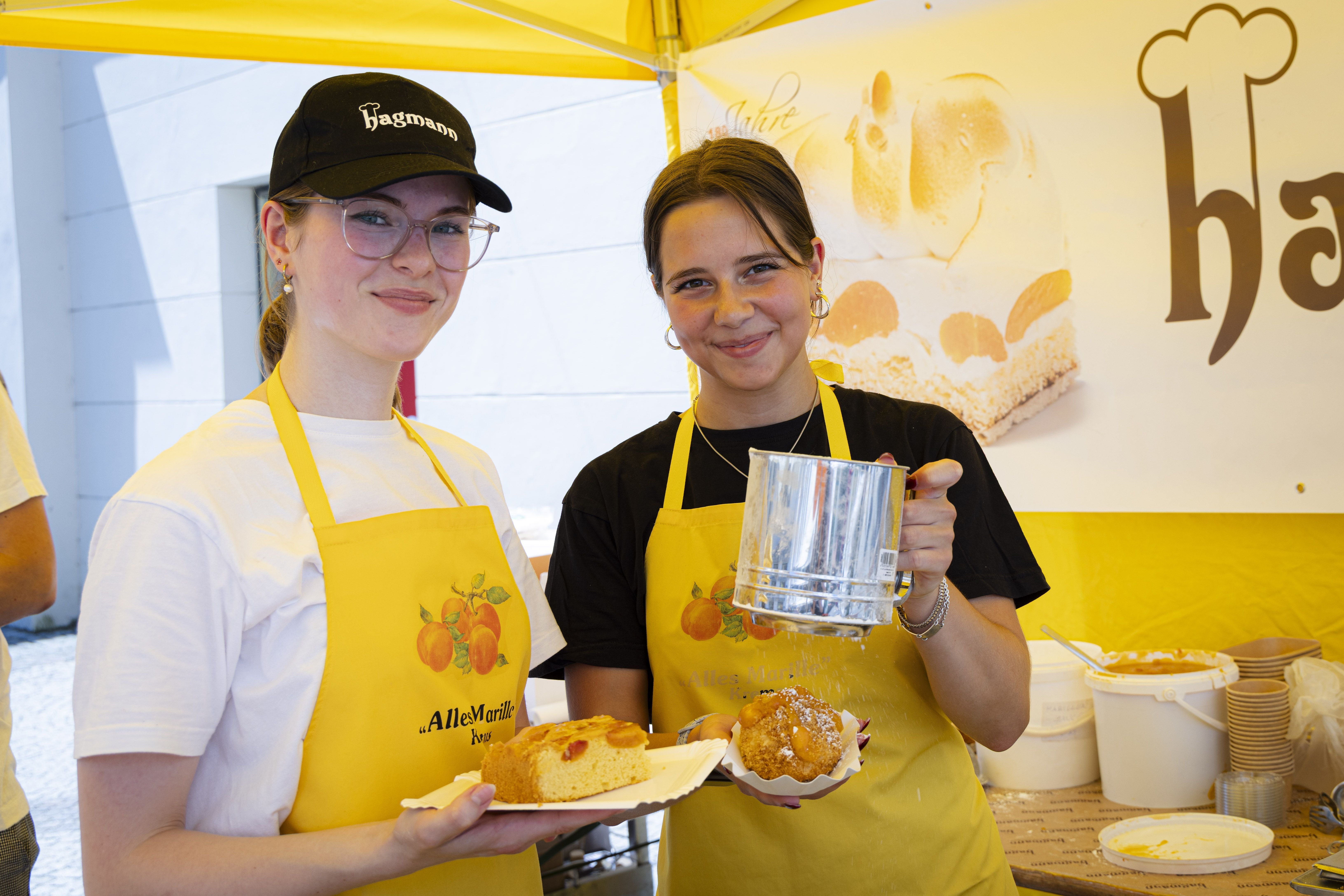 Zwei Personen mit gelben Schürzen bieten Aprikosenkuchen auf einem Straßenfest an.