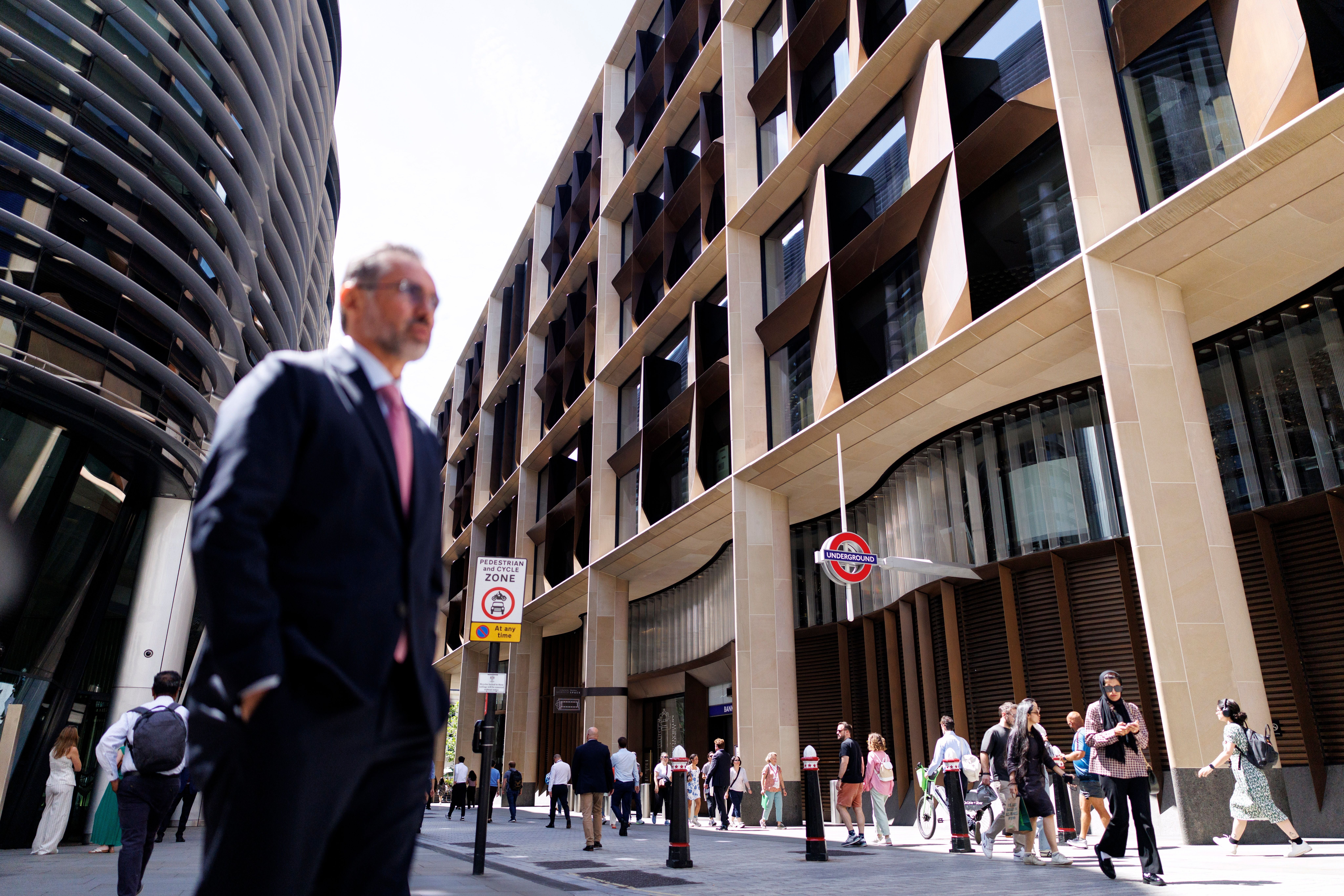 Menschen laufen in der City of London vor modernen Bürogebäuden bei sonnigem Wetter.