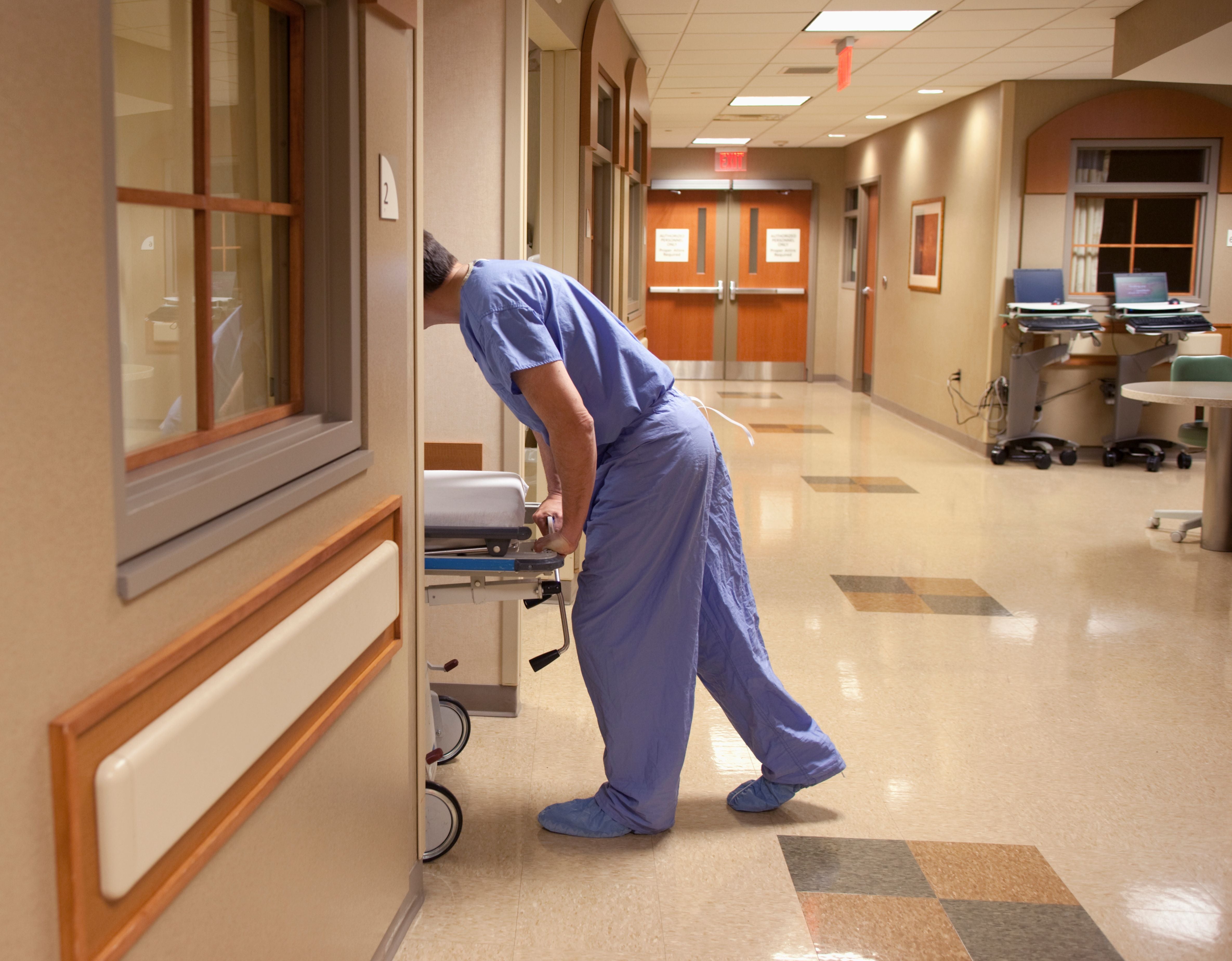 Ein Pflegekraft schiebt ein Patientenbett in ein Krankenzimmer in einem Krankenhausflur.