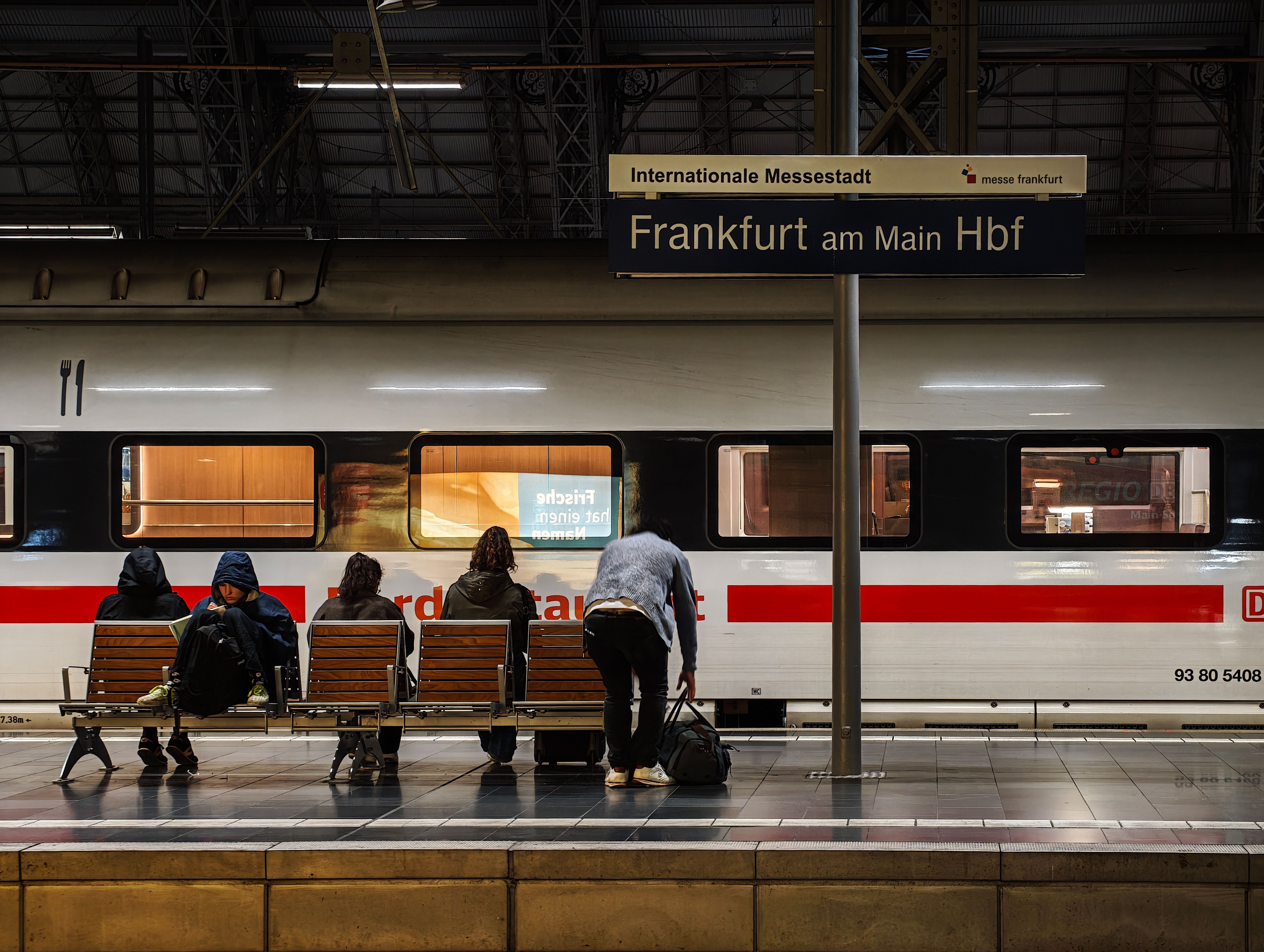 Fünf Menschen warten auf Bänken am Bahnsteig im Hauptbahnhof Frankfurt am Main vor einem ICE-Zug.