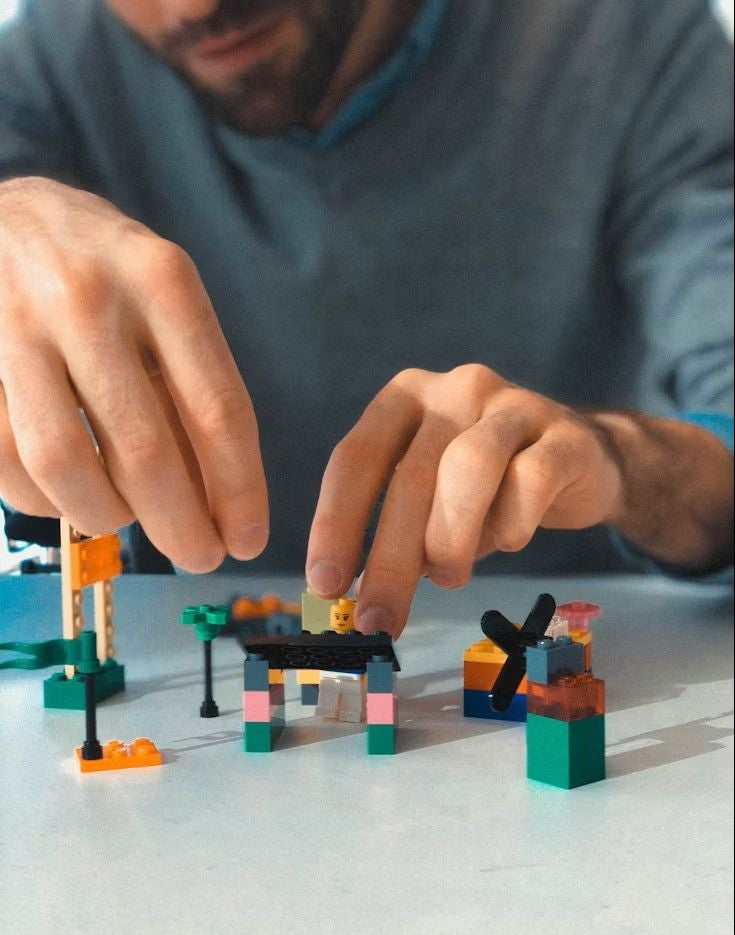 Eine Person baut kleine bunte Lego-Prototypen mit den Händen auf einem Tisch.