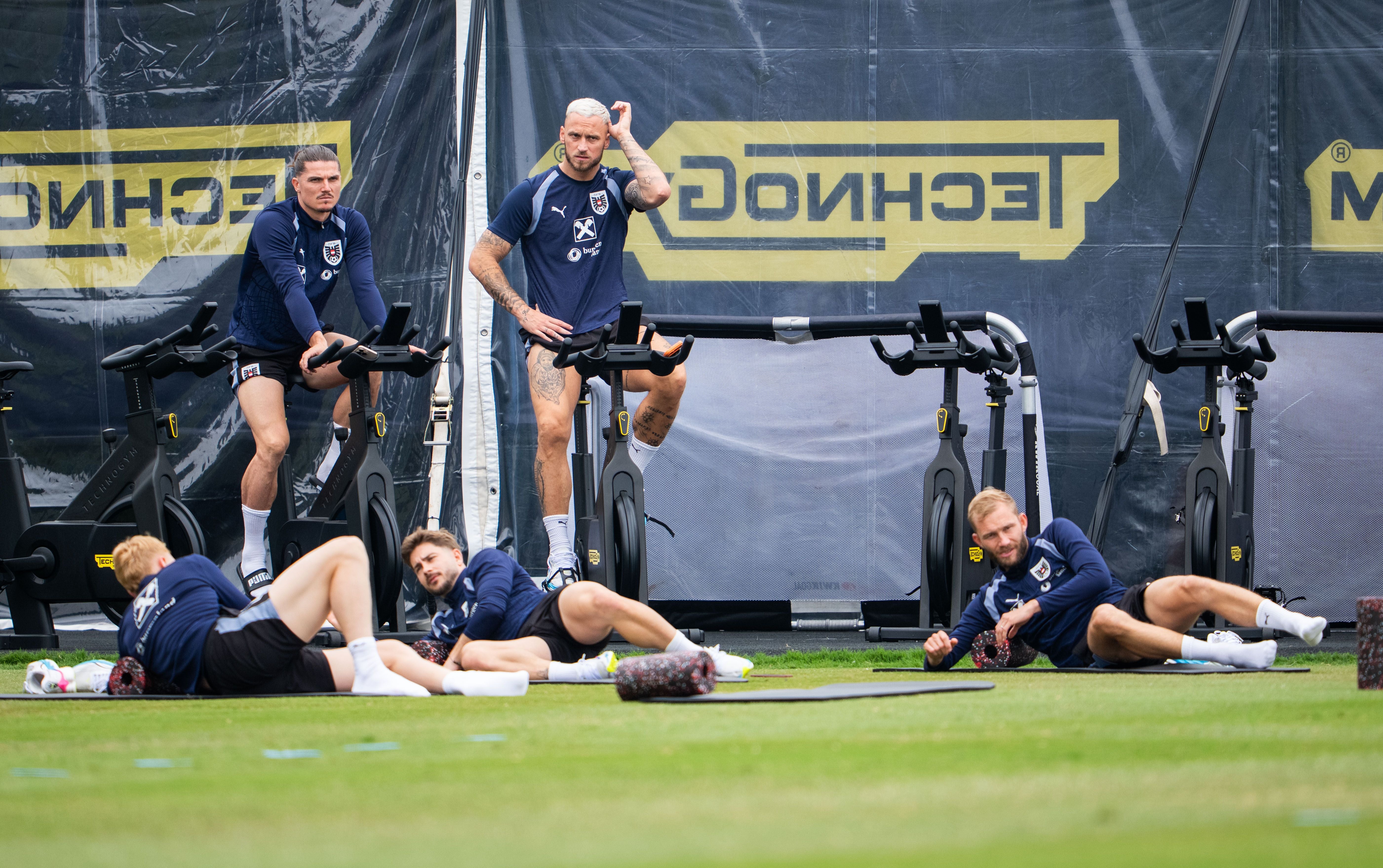 Mehrere Fußballspieler trainieren gemeinsam auf Fahrradergometern und Matten im Freien.