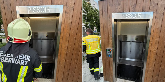 Zwei Feuerwehrleute stehen vor einem öffentlichen Pissoir aus Holz und Metall.