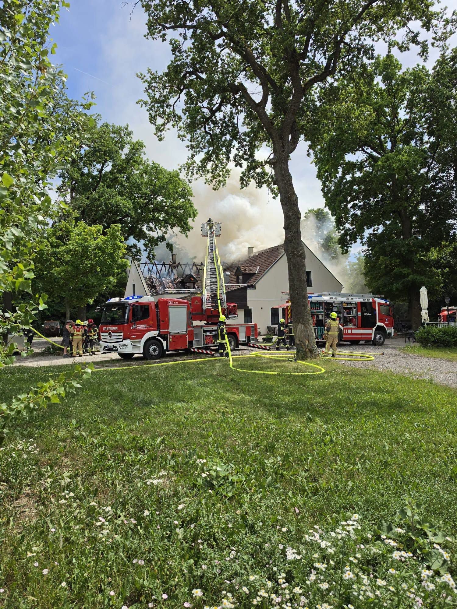 Ein brennendes Gasthaus, Feuerwehrleute und mehrere Einsatzfahrzeuge löschen den Brand.