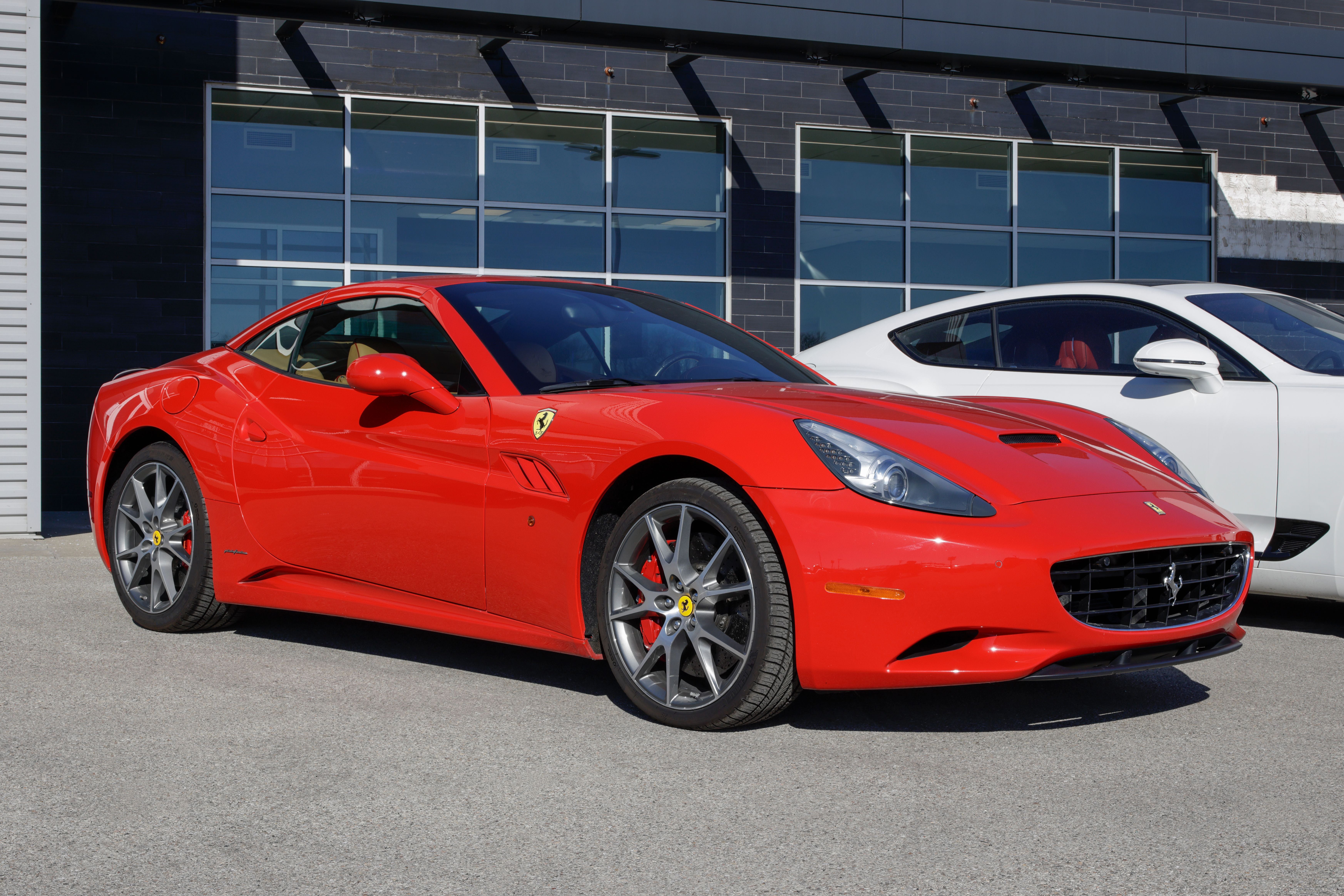 Roter Ferrari California Base von 2011 steht vor einem Autohaus neben einem weißen Fahrzeug.