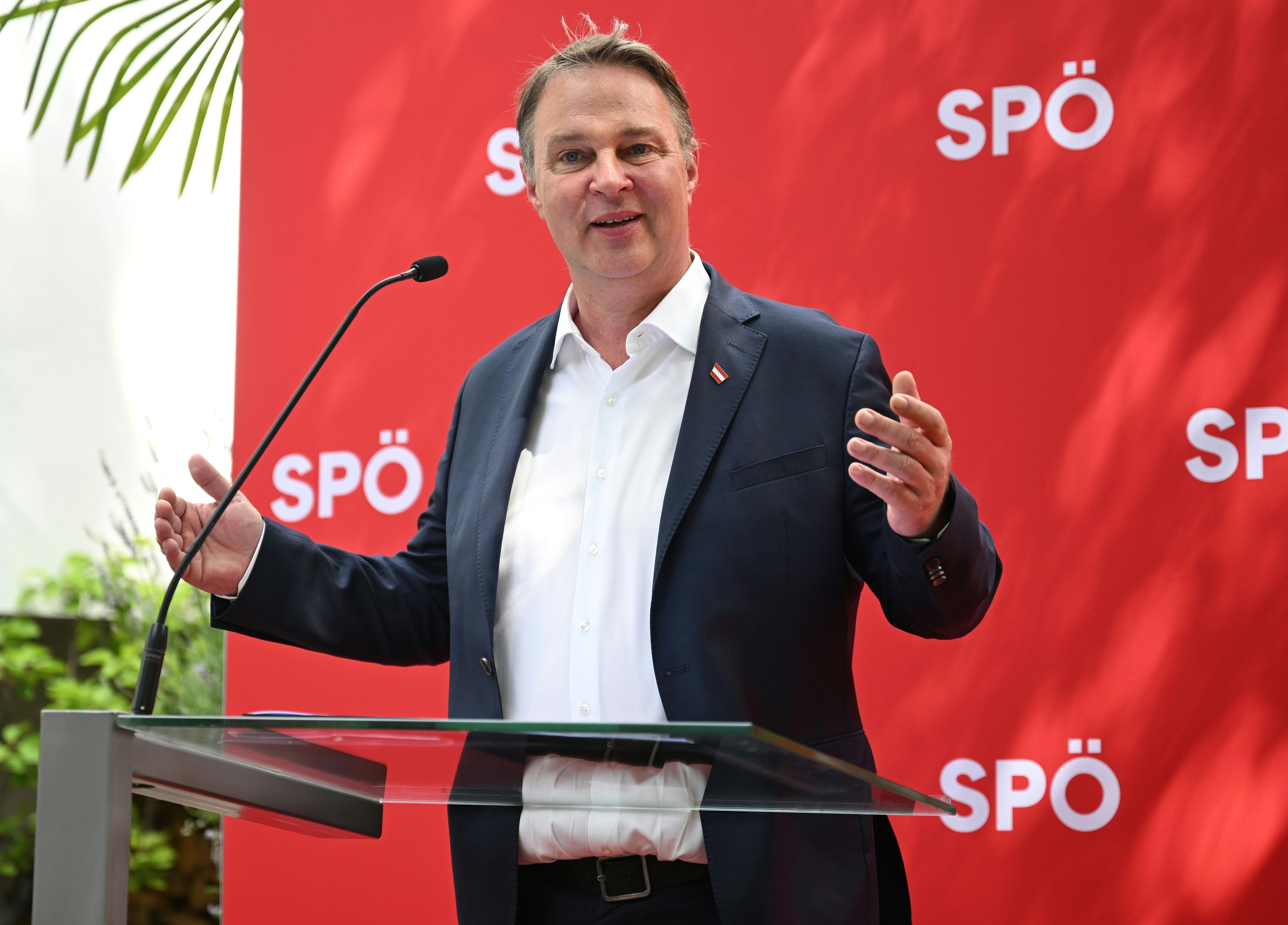 Ein Mann im Anzug spricht auf einer Pressekonferenz vor SPÖ-Hintergrund mit Mikrofon.