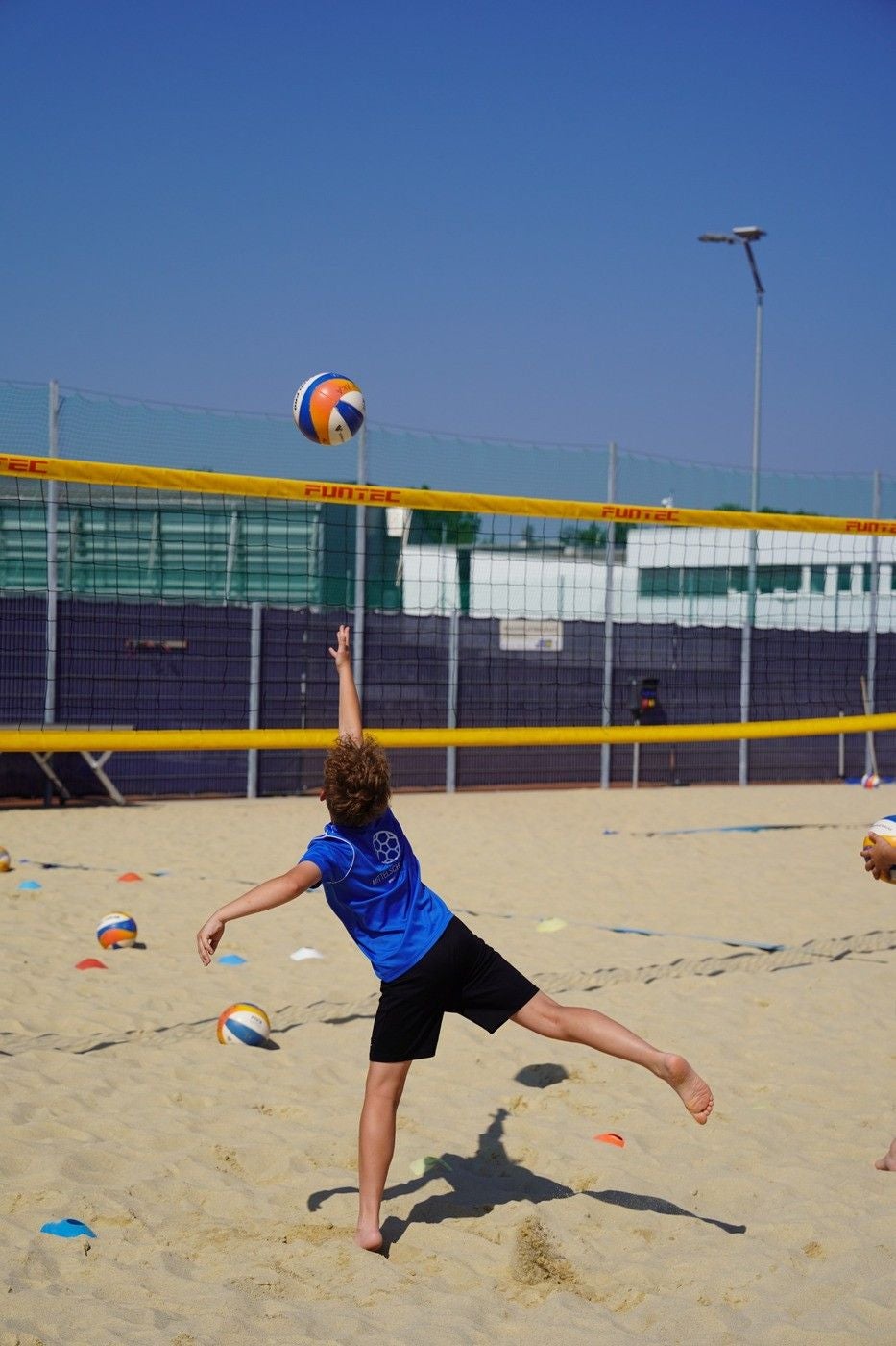 Ein Kind spielt Beachvolleyball und schlägt den Ball über das Netz auf einem Sandplatz.