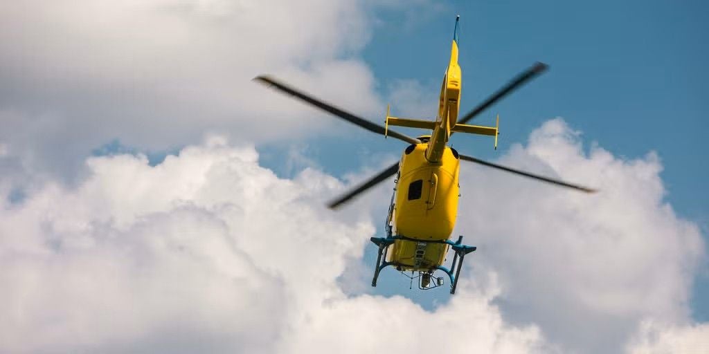 Gelber Rettungshubschrauber fliegt vor bewölktem Himmel in Richtung Kamera.