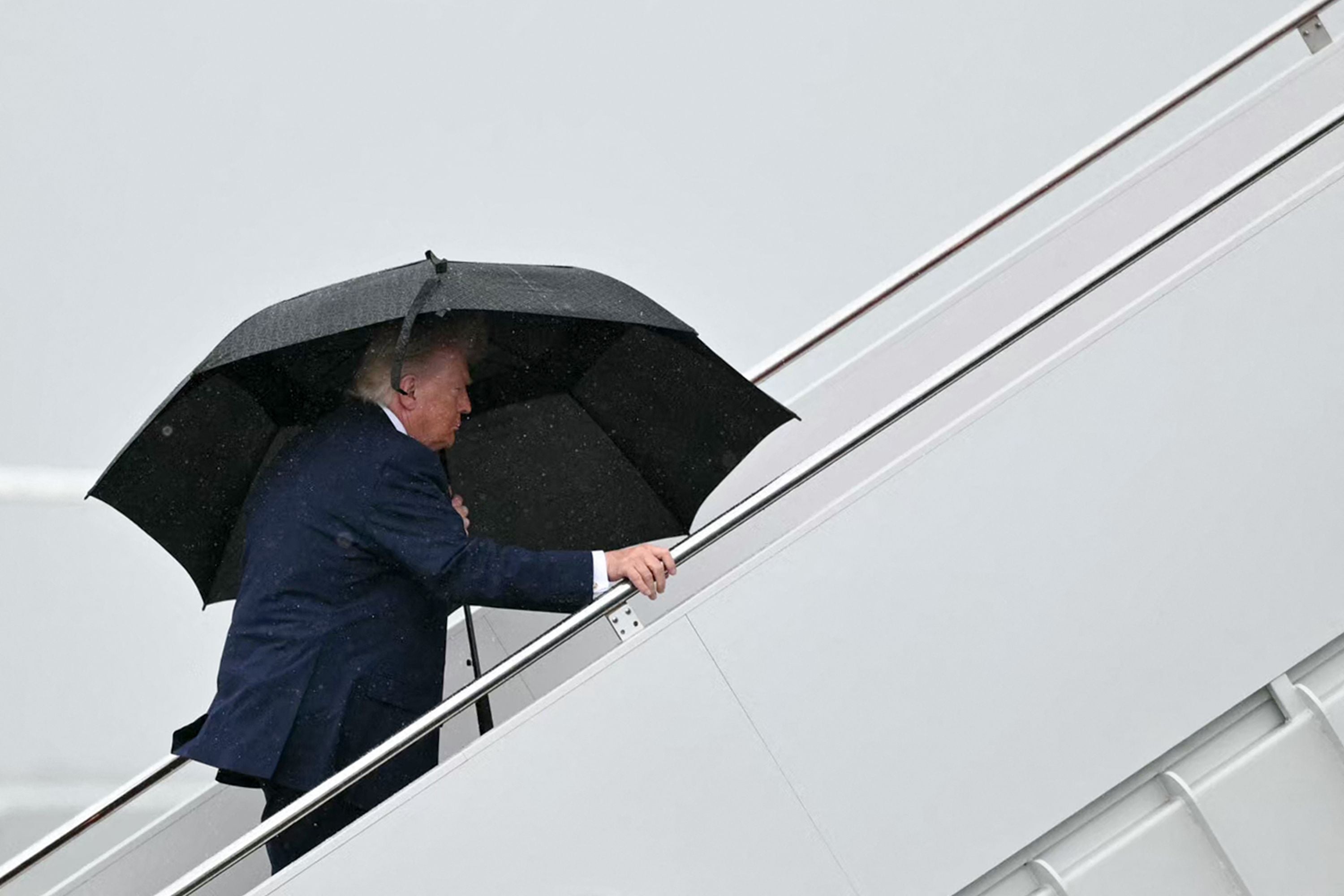 Ein Mann mit Regenschirm besteigt im Regen eine Flugzeugtreppe.
