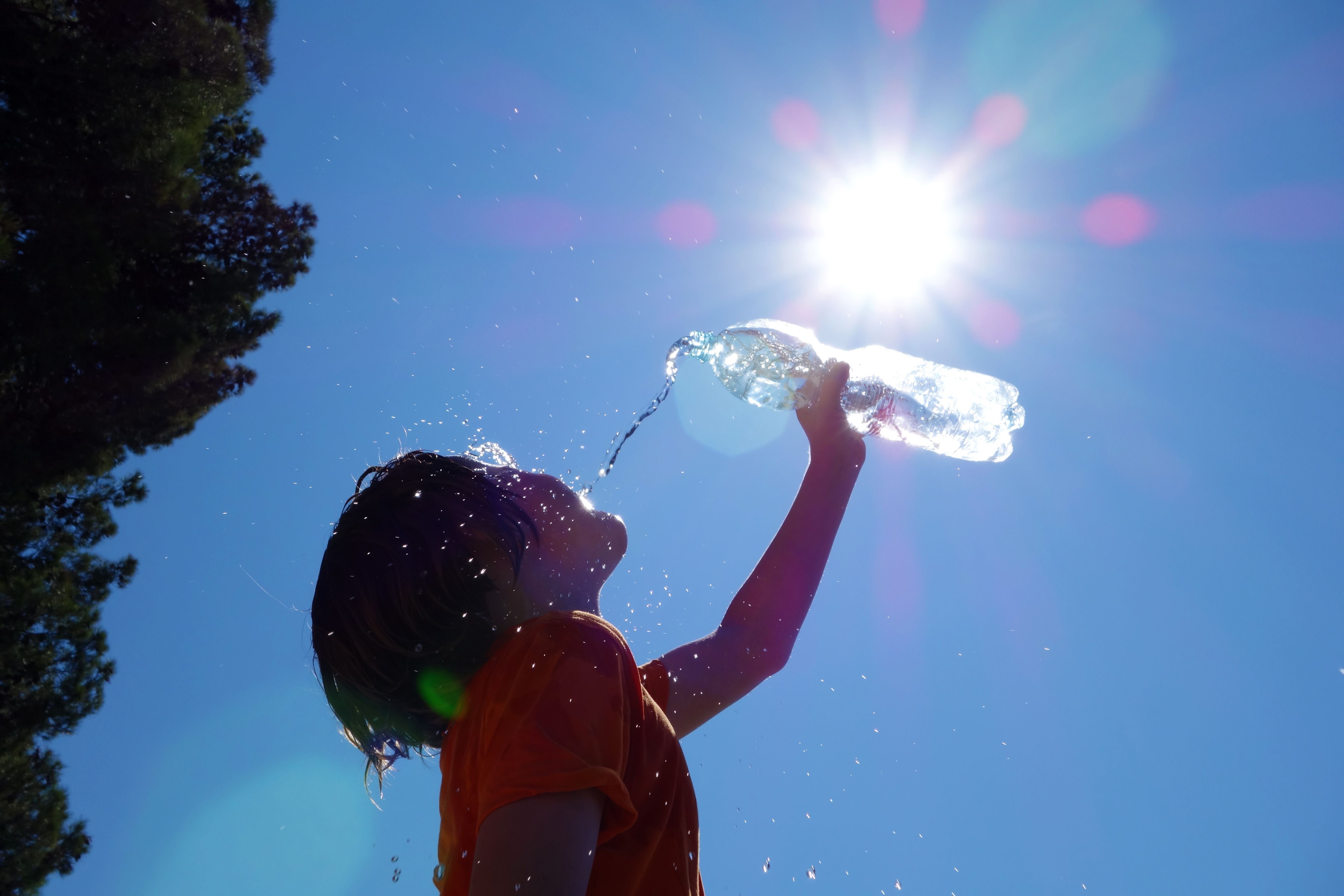 Kind gießt sich bei Sonnenschein Wasser aus einer Flasche über den Kopf.