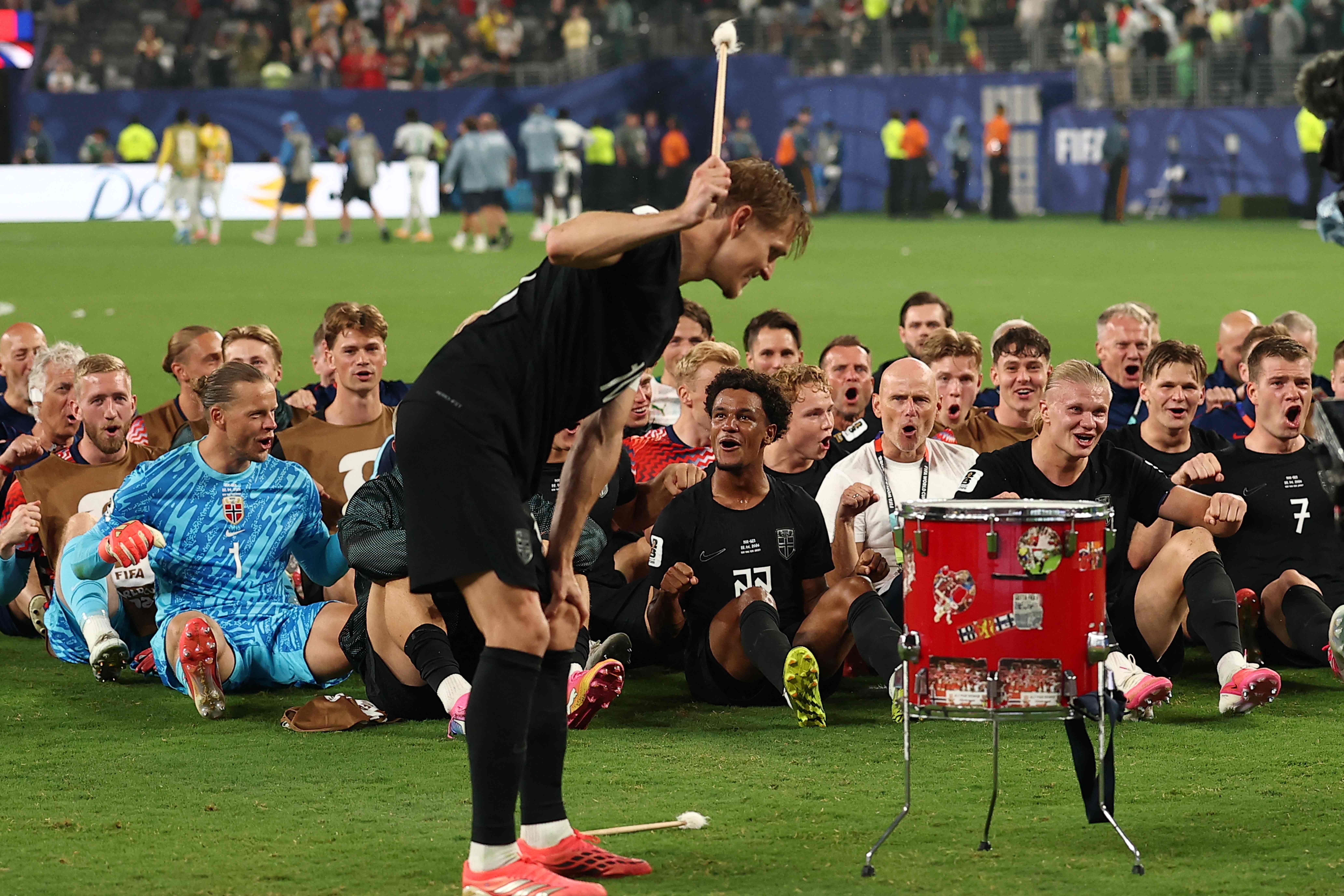 Norwegische Fußballspieler feiern sitzend, während ein Spieler auf einer Trommel schlägt.