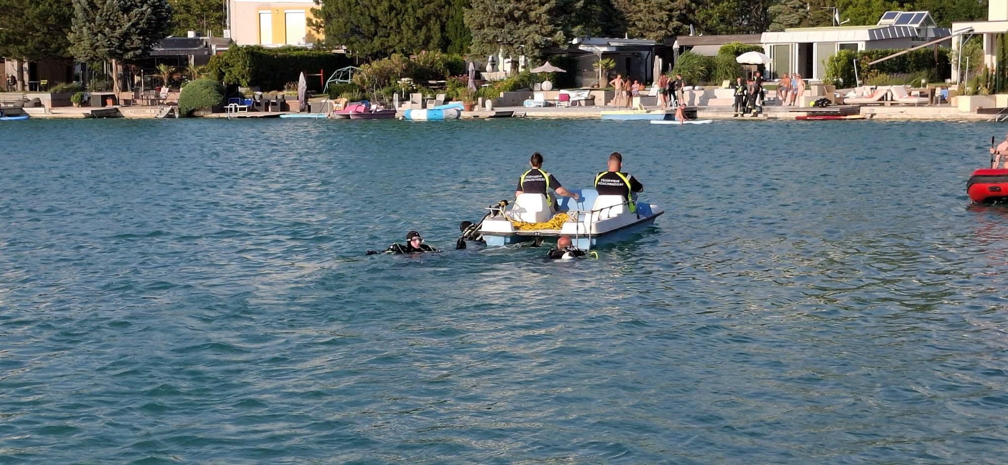 Zwei Rettungskräfte auf einem Tretboot, zwei Taucher im Wasser eines Sees bei Münchendorf.