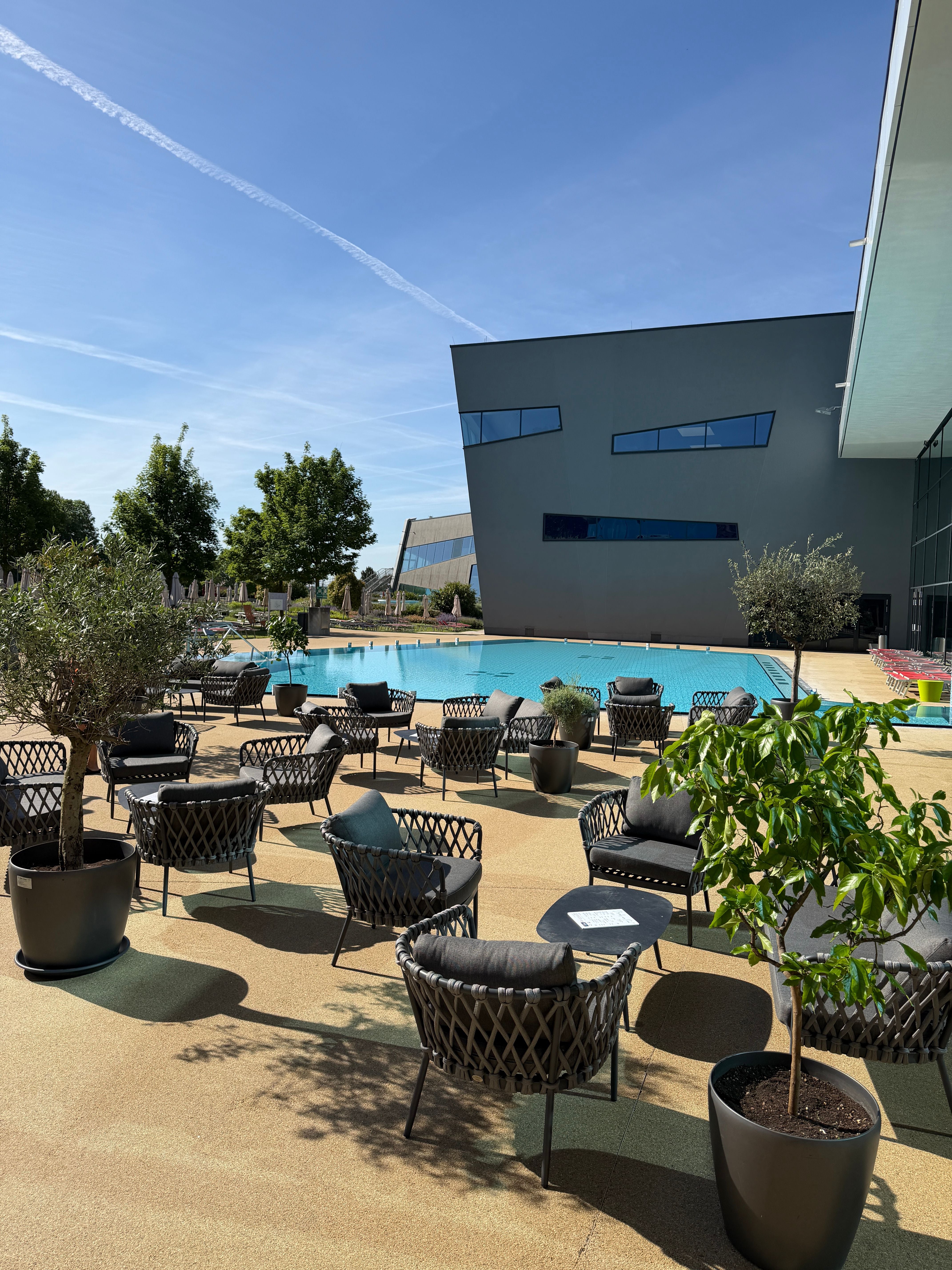 Terrasse der Therme Wien mit modernen Sitzgruppen und Pflanzen am Pool bei sonnigem Wetter.