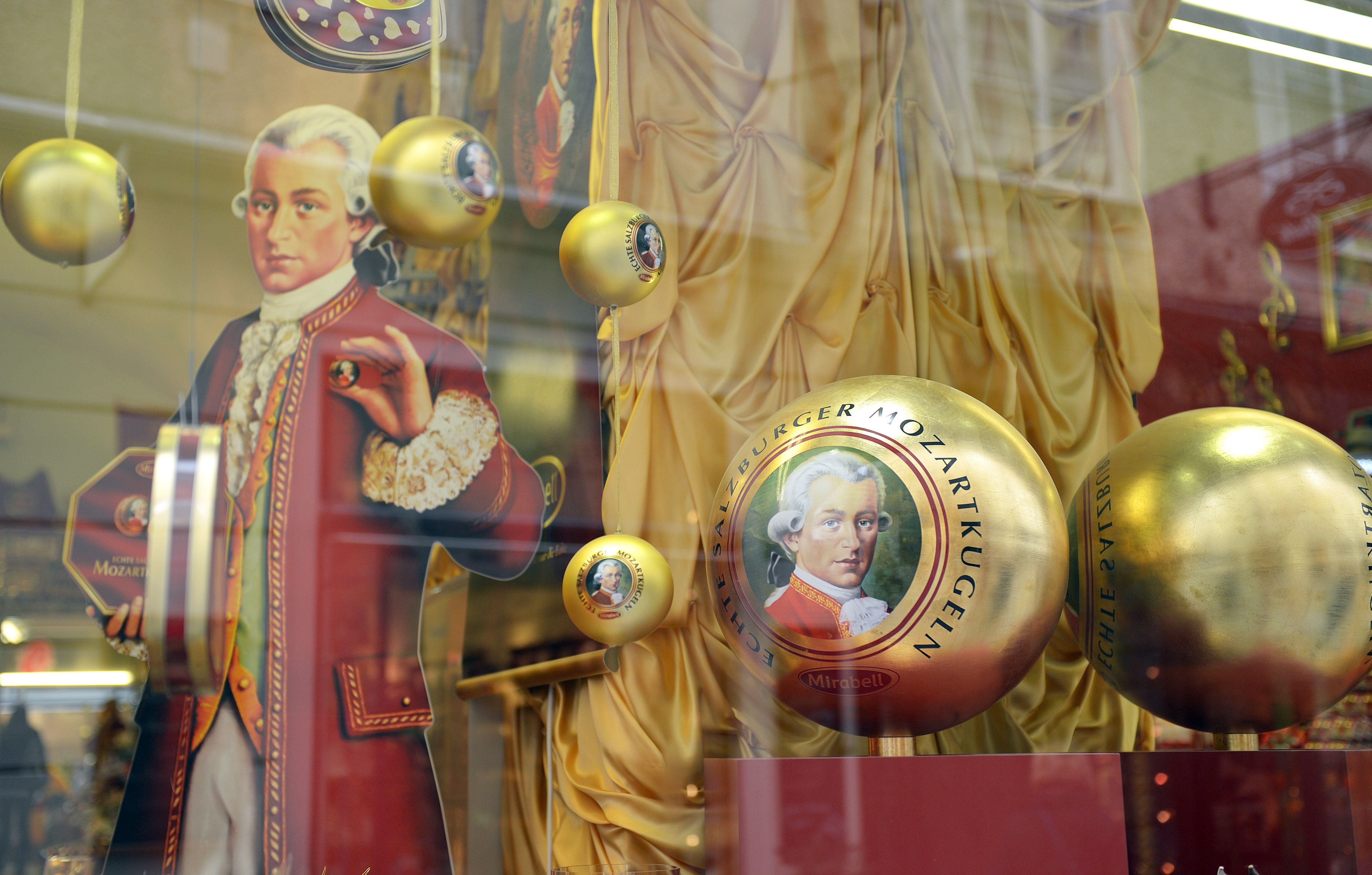 Schaufenster mit goldenen Salzburger Mozartkugeln und einer Figur in historischer Kleidung.