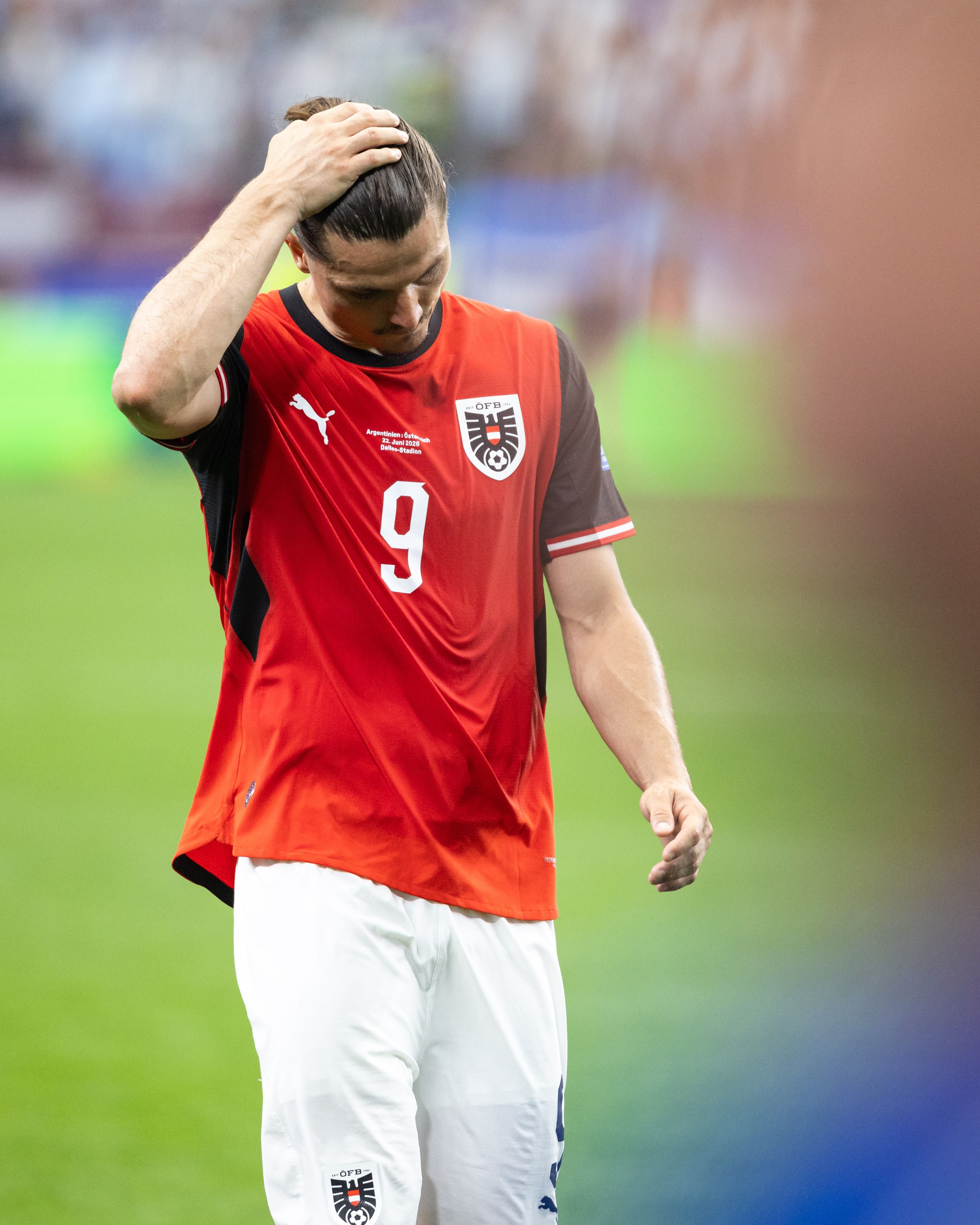 Ein österreichischer Fußballer im roten Trikot wirkt enttäuscht und fasst sich an den Kopf.
