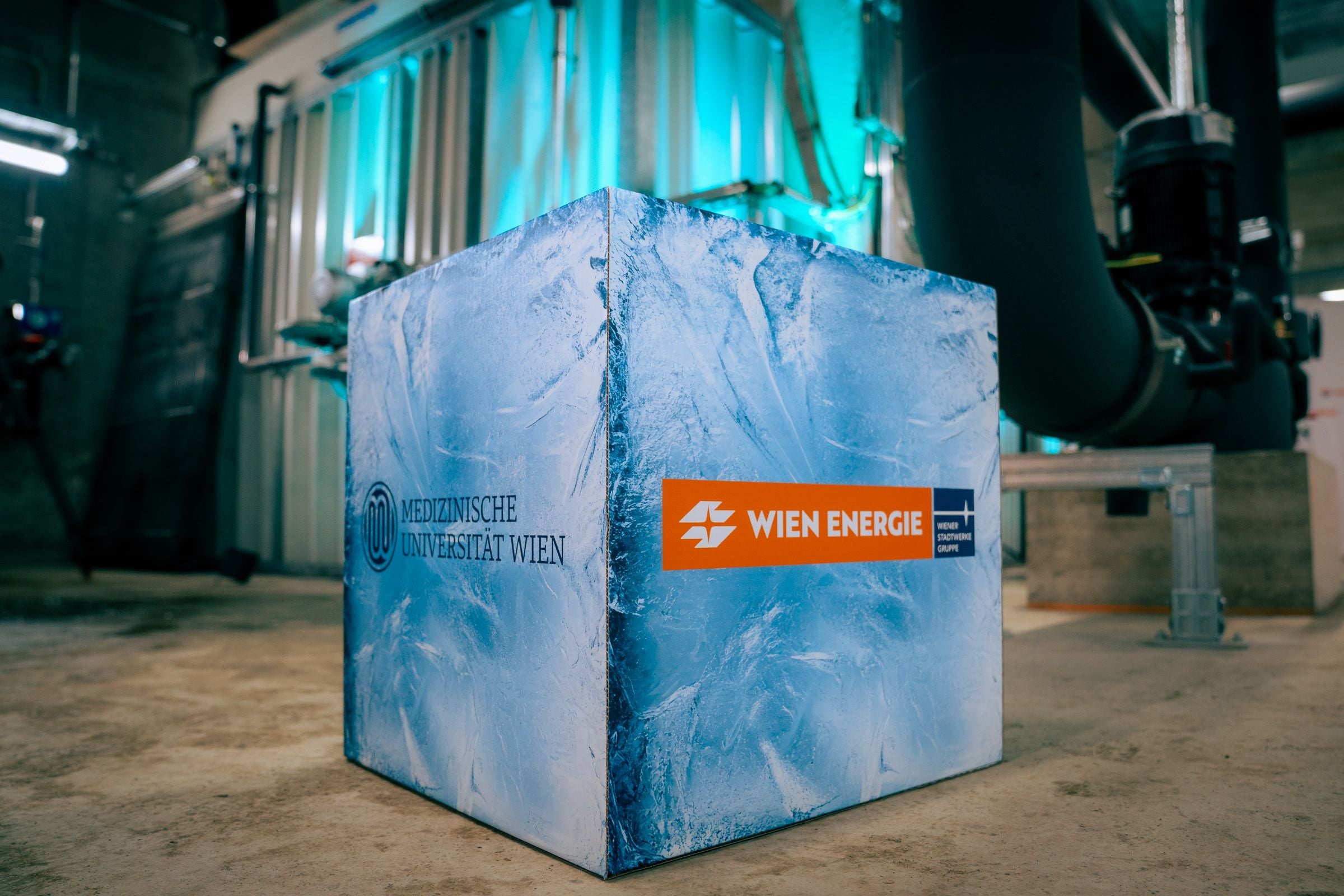 Würfelförmiger Eisspeicher mit Logos von MedUni Wien und Wien Energie in einer technischen Anlage.