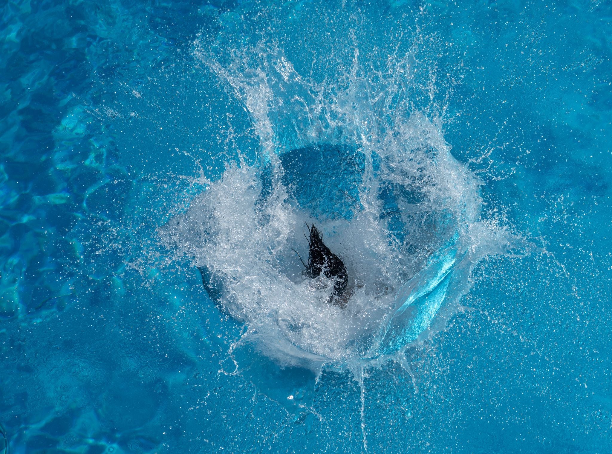Spritzendes Wasser in einem Pool, nur Haarspitzen einer springenden Frau sind sichtbar.