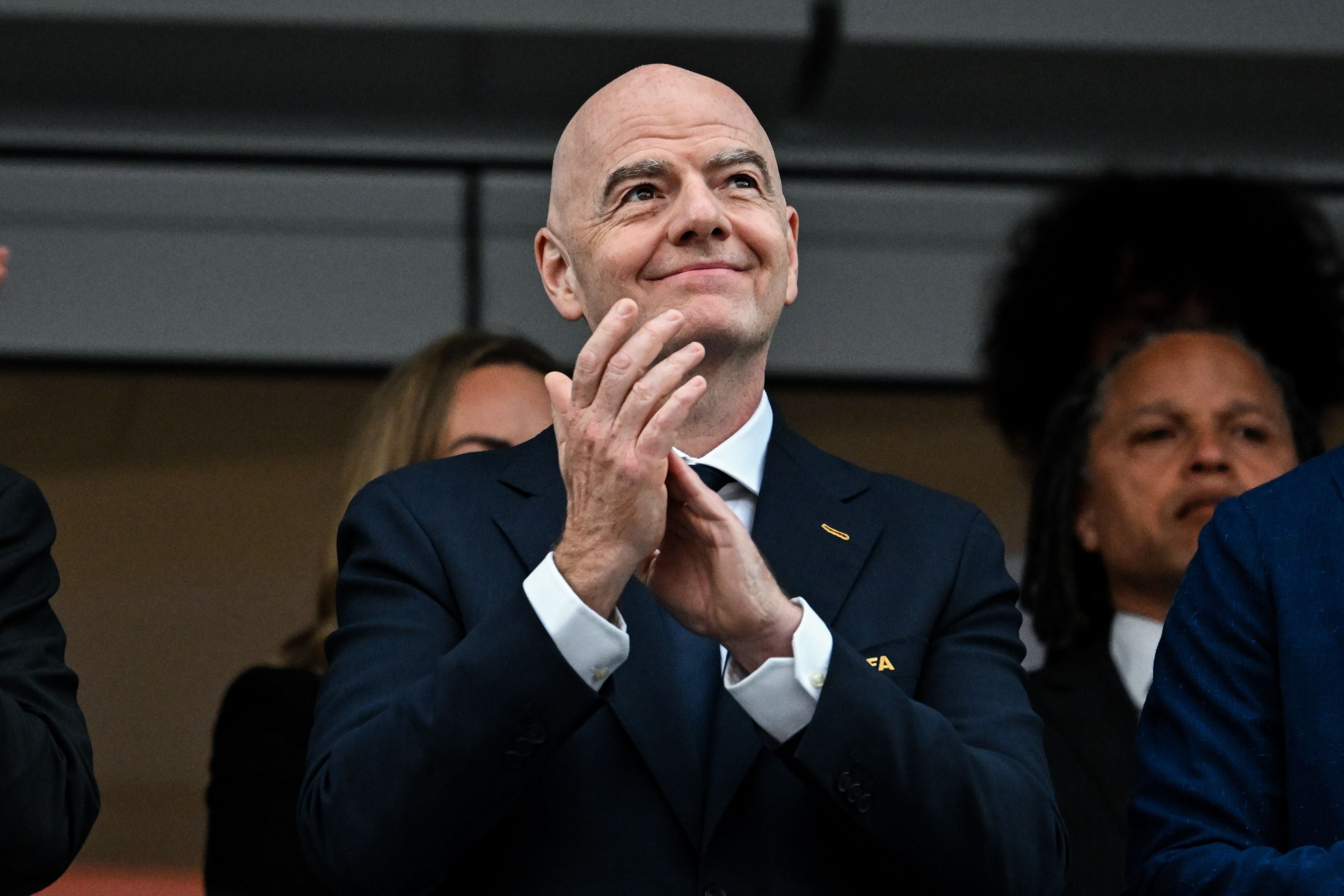 Ein Mann im Anzug klatscht auf einer Tribüne bei einem Fußballspiel.