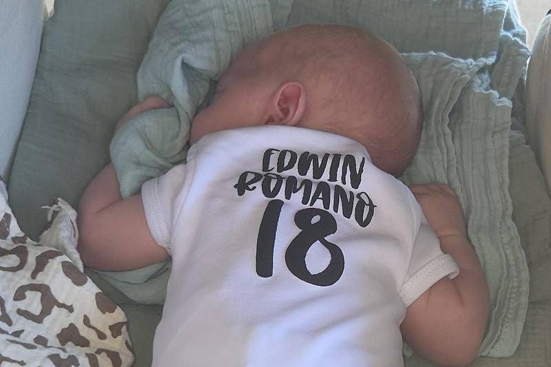 Baby liegt auf dem Bauch und trägt einen Body mit der Aufschrift "Edwin Romano 18".
