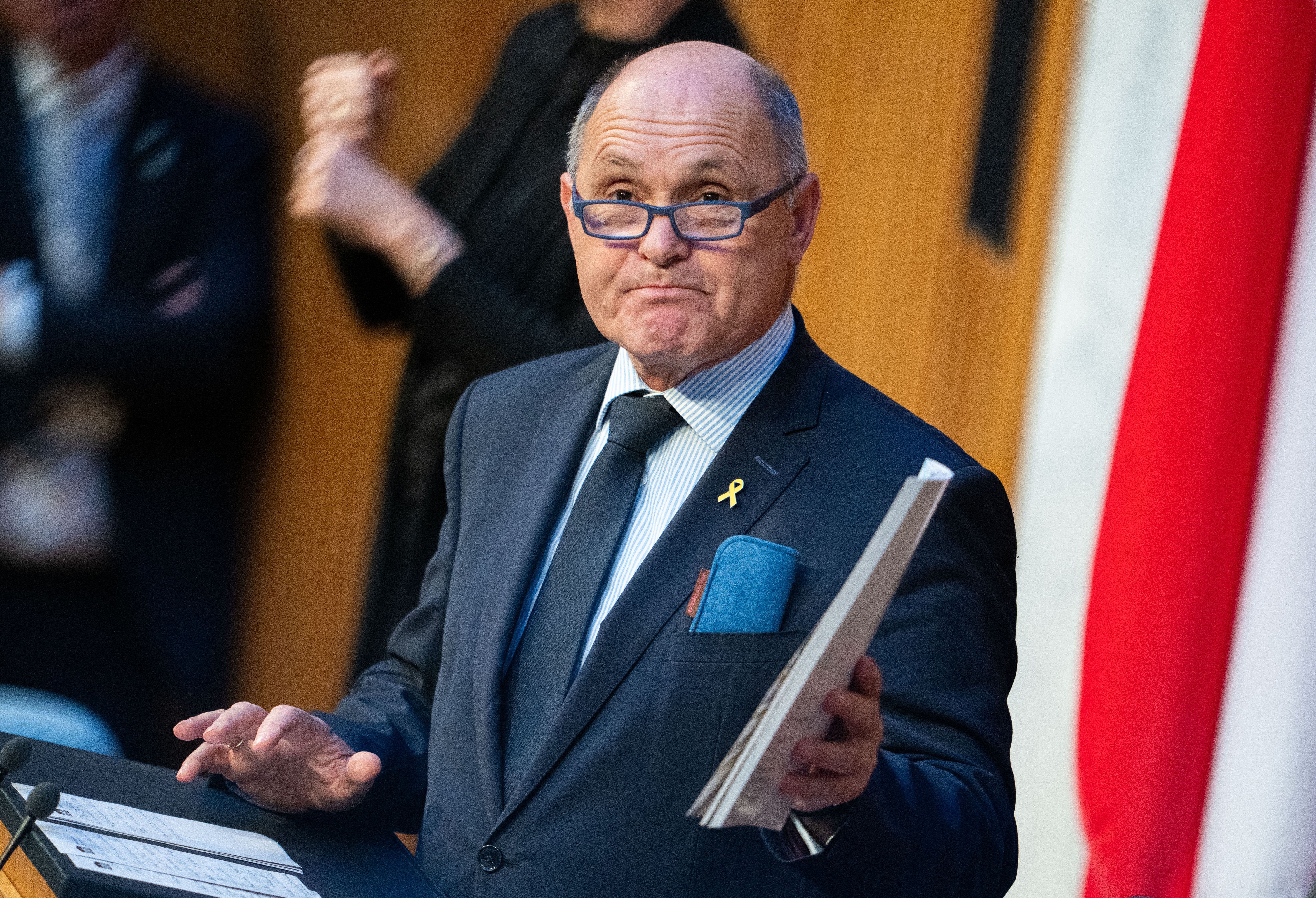 Ein Mann im Anzug spricht am Rednerpult und hält Unterlagen in der Hand.