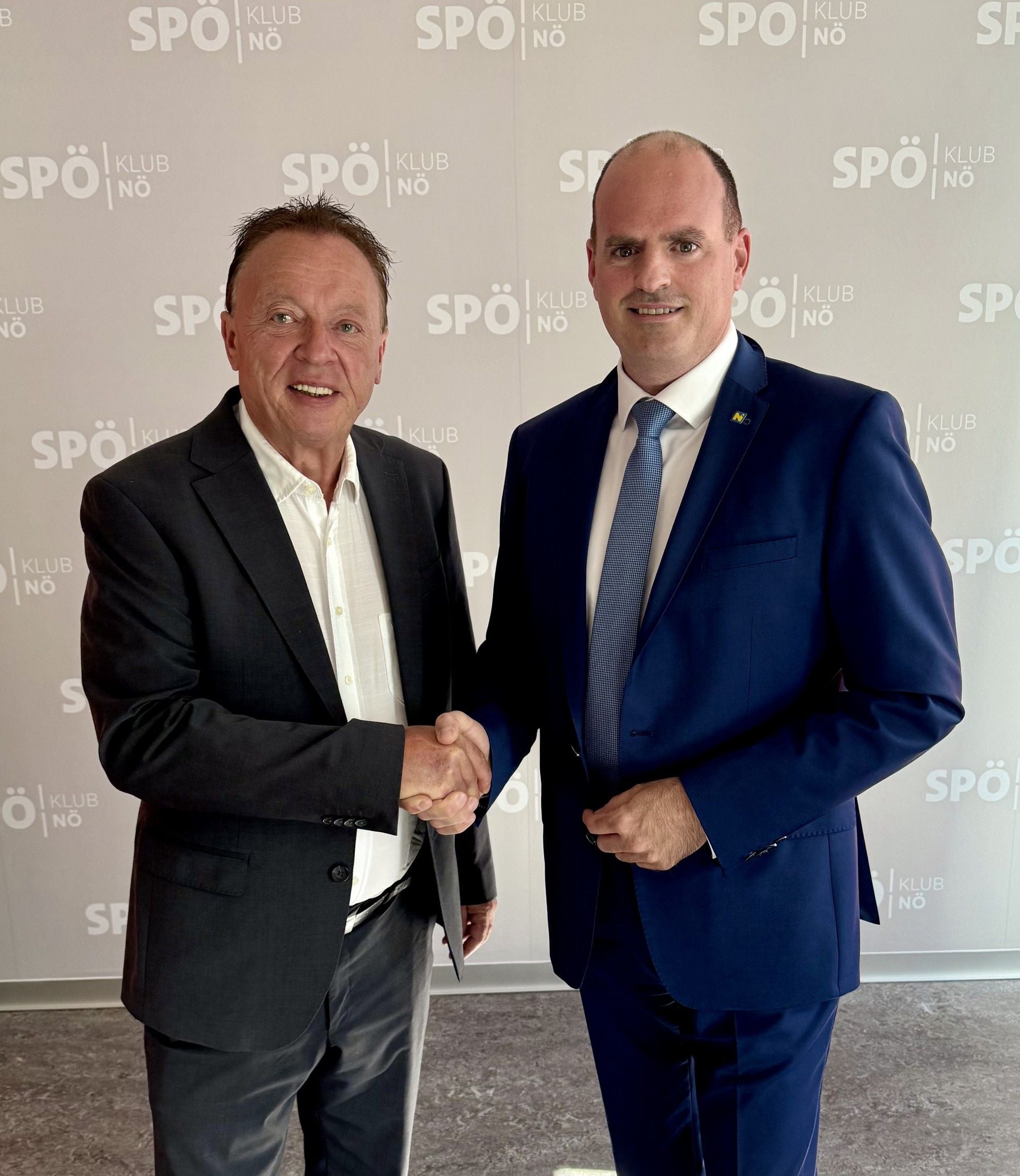 Zwei Männer in Anzügen geben sich vor SPÖ-Hintergrund die Hand.