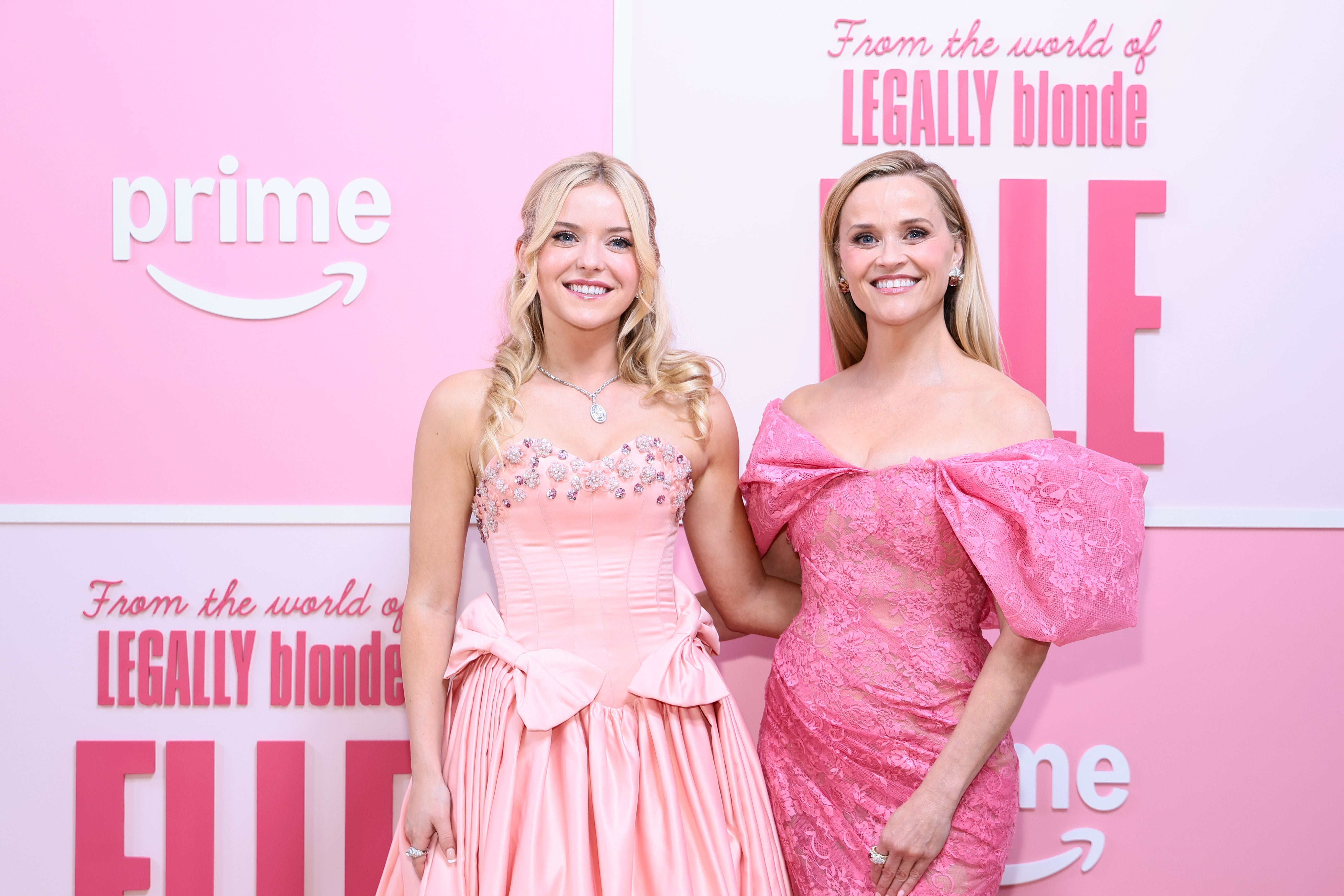 Zwei Frauen in eleganten, pinken Kleidern posieren vor einer "Legally Blonde Elle"-Premierenwand.