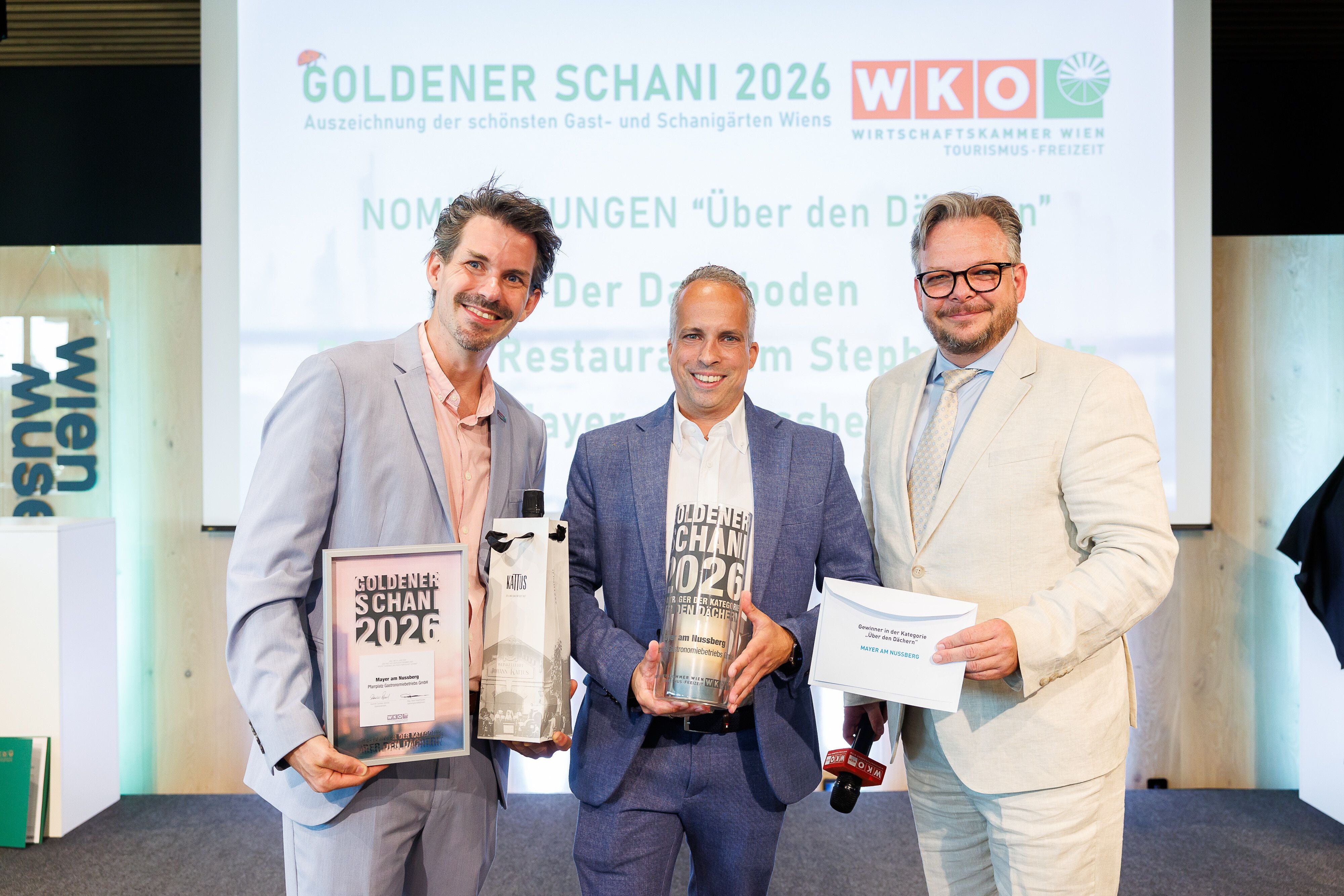 Drei Männer im Anzug posieren mit Urkunde und Trophäe bei der Goldener Schani 2026 Preisverleihung.