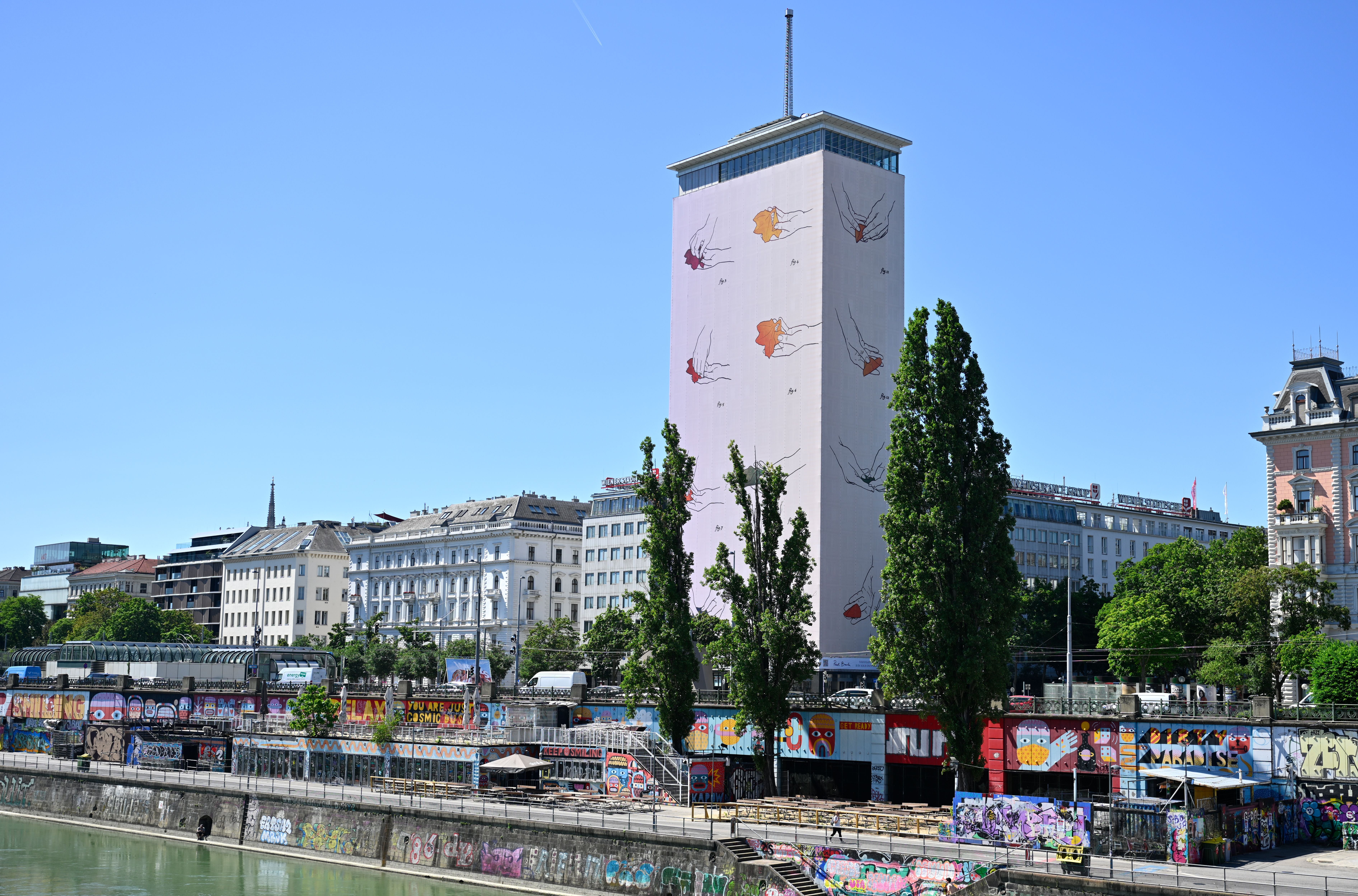 Der Wiener Ringturm mit Kunstverhüllung und Graffiti am Donaukanal bei sonnigem Wetter.