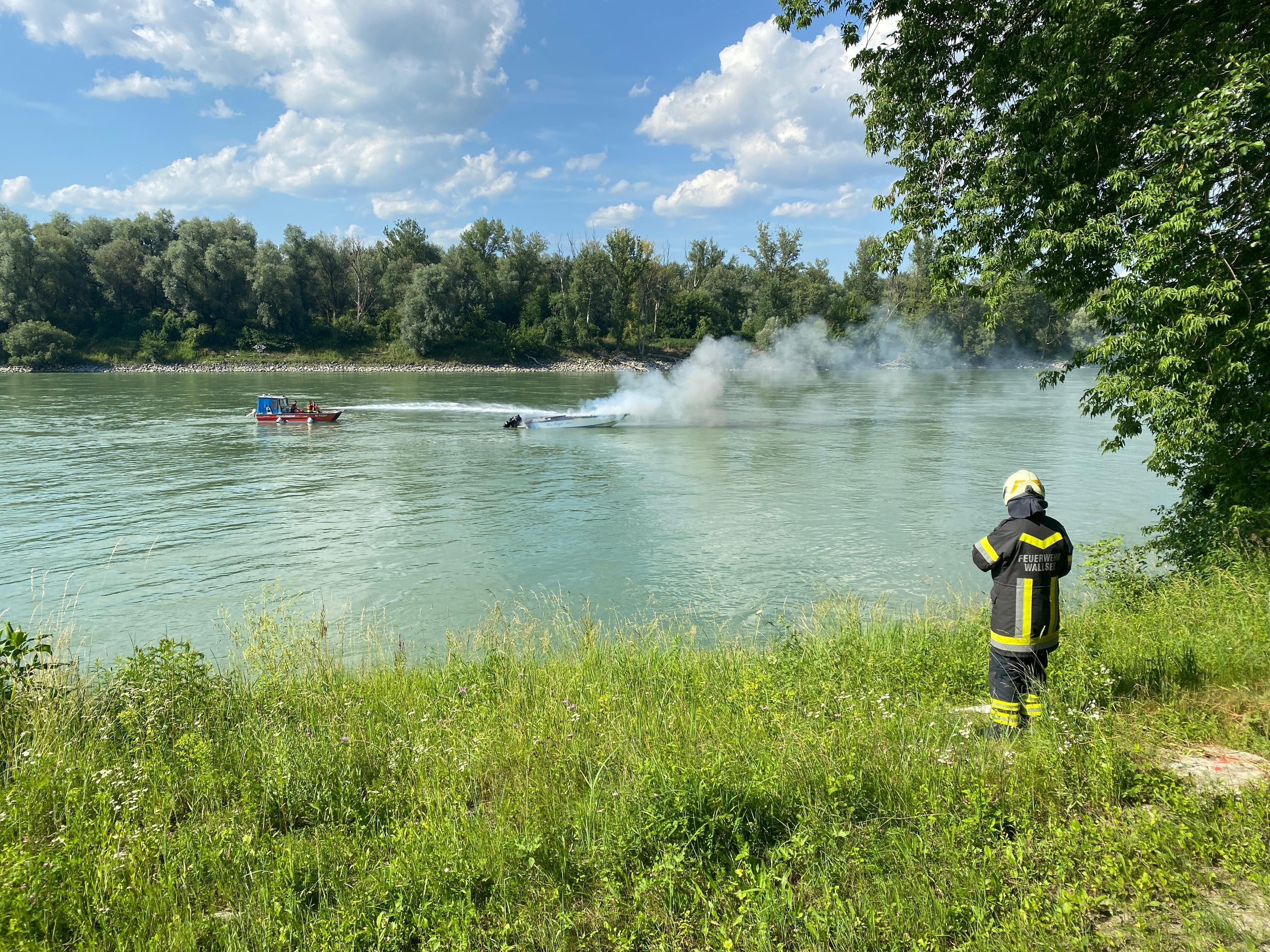 Ein Feuerwehrmann beobachtet ein Feuerwehrboot, welches das brennende Sportboot auf der Donau löscht.