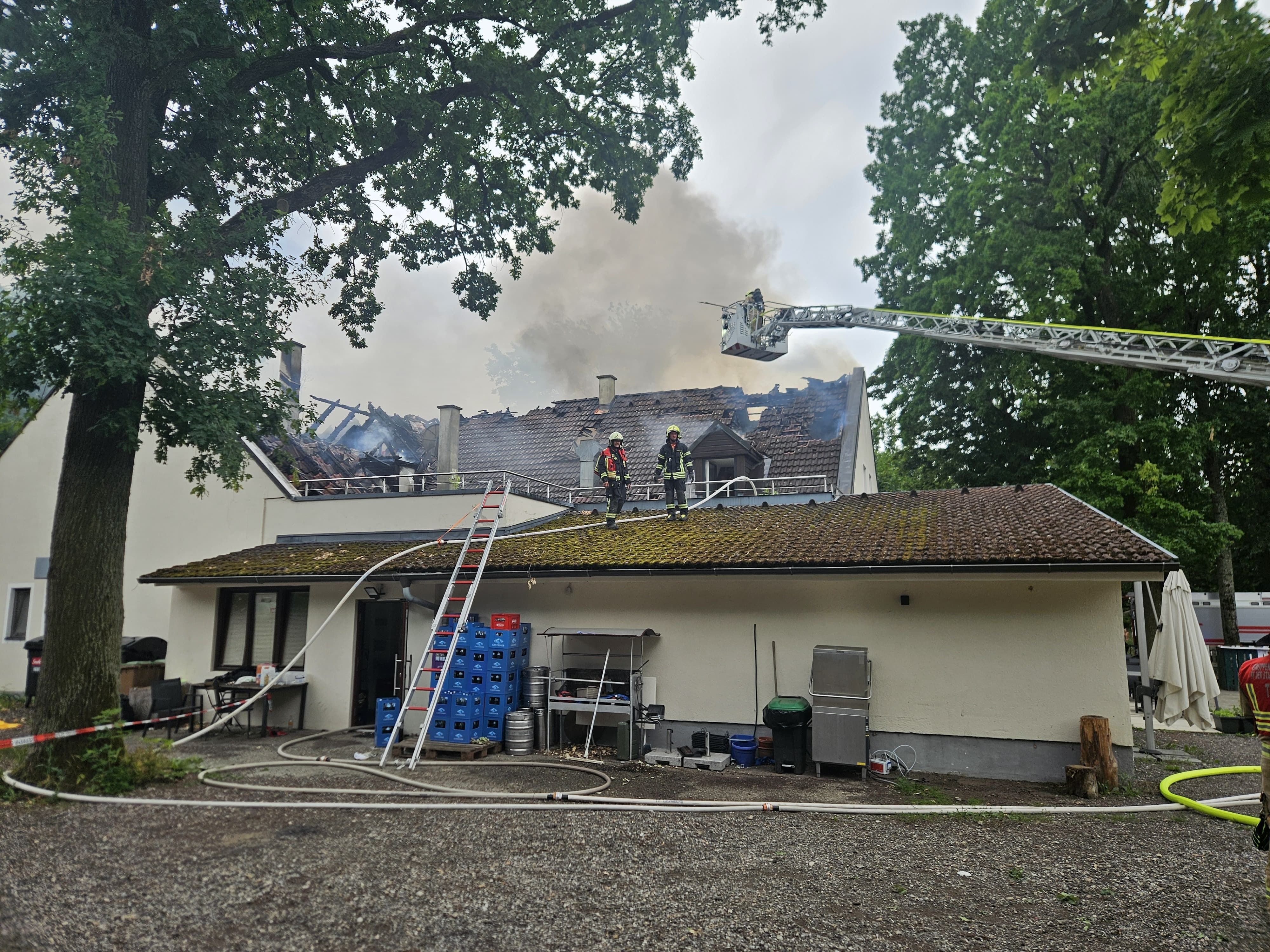 Feuerwehrleute löschen einen Brand auf dem Dach eines Gasthauses, dichter Rauch steigt auf.