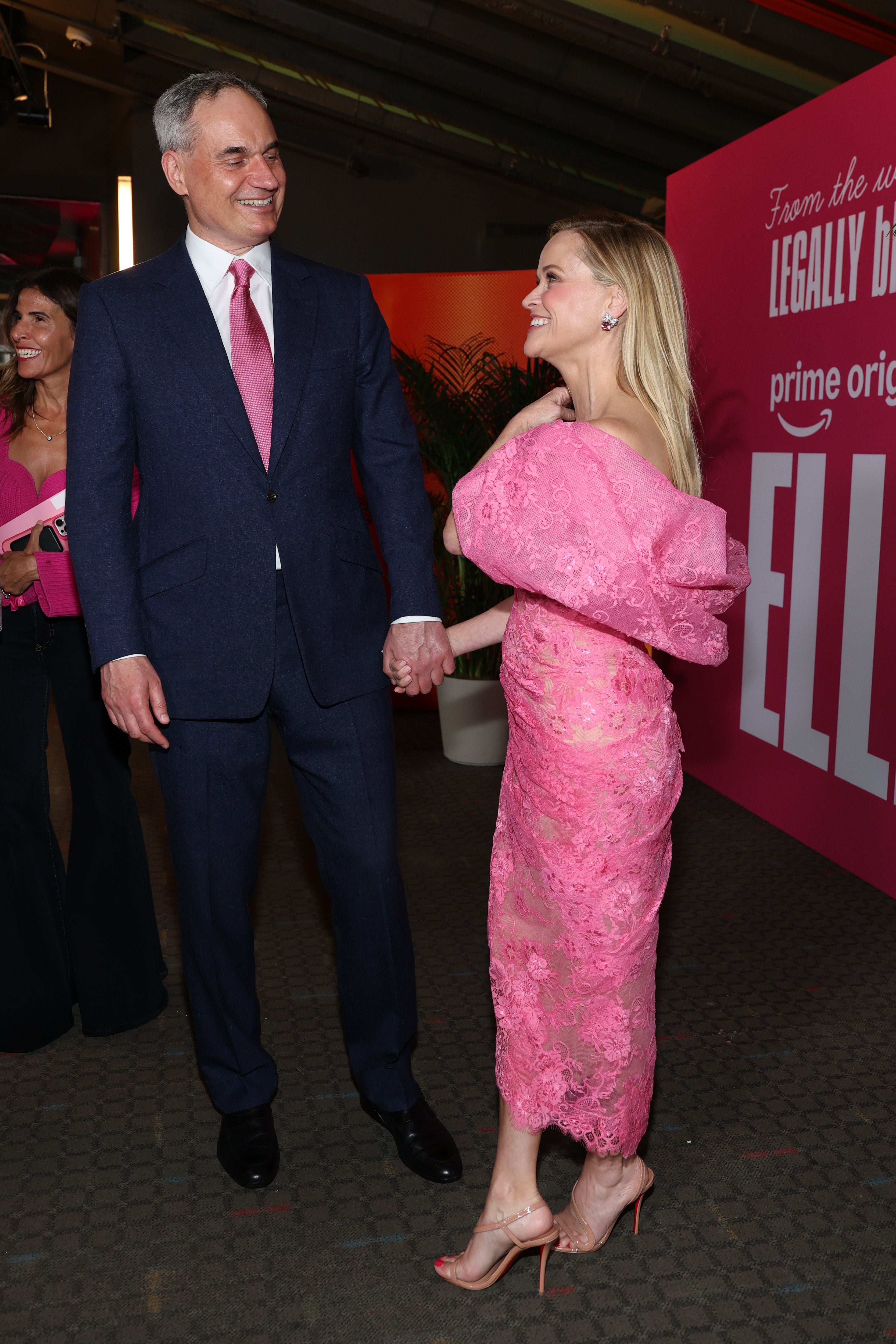 Ein Mann im Anzug und eine Frau im rosa Kleid halten Händchen bei einer Premierenveranstaltung.