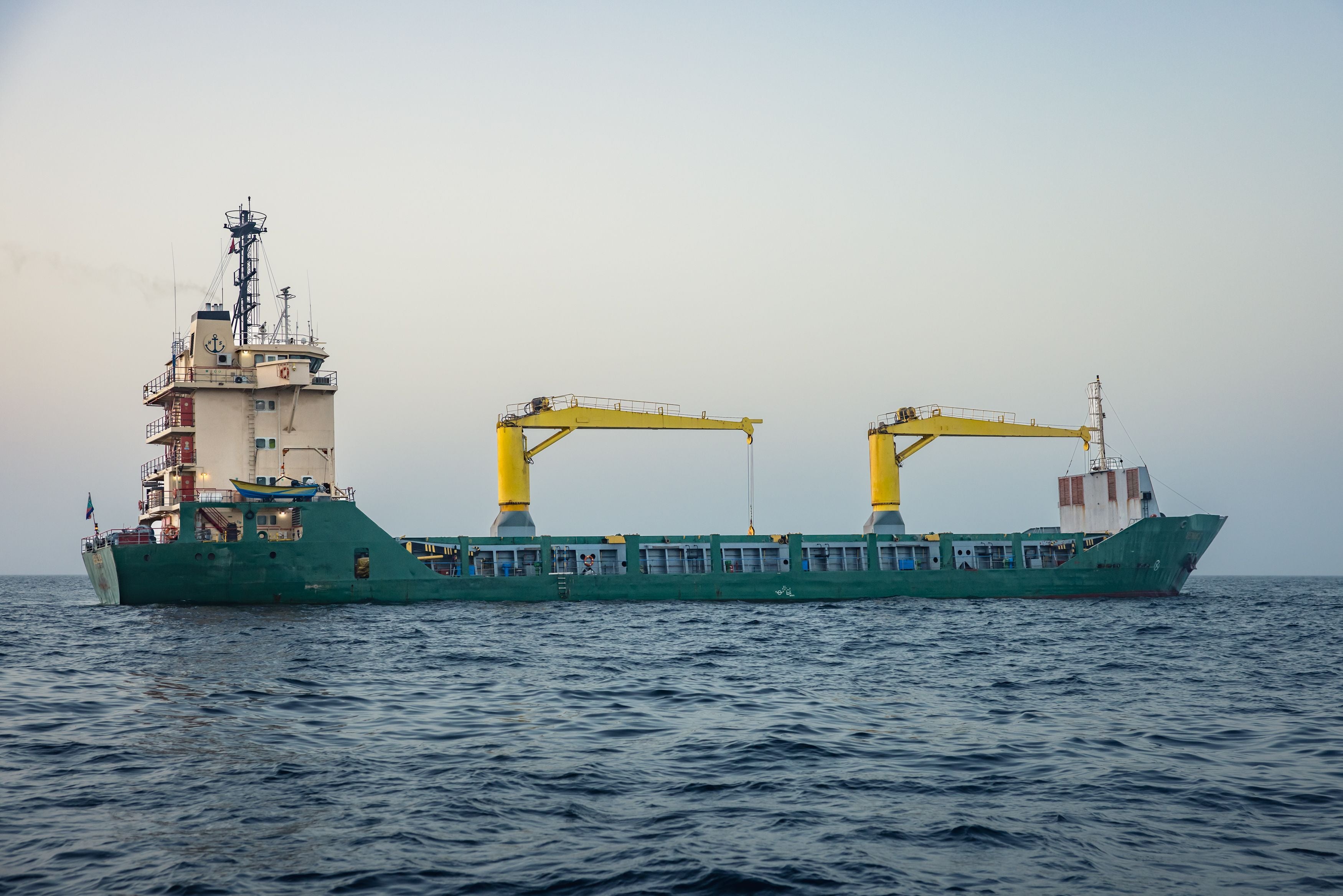Ein Frachtschiff mit zwei gelben Kränen liegt vor Anker auf ruhigem Meer nahe Oman.
