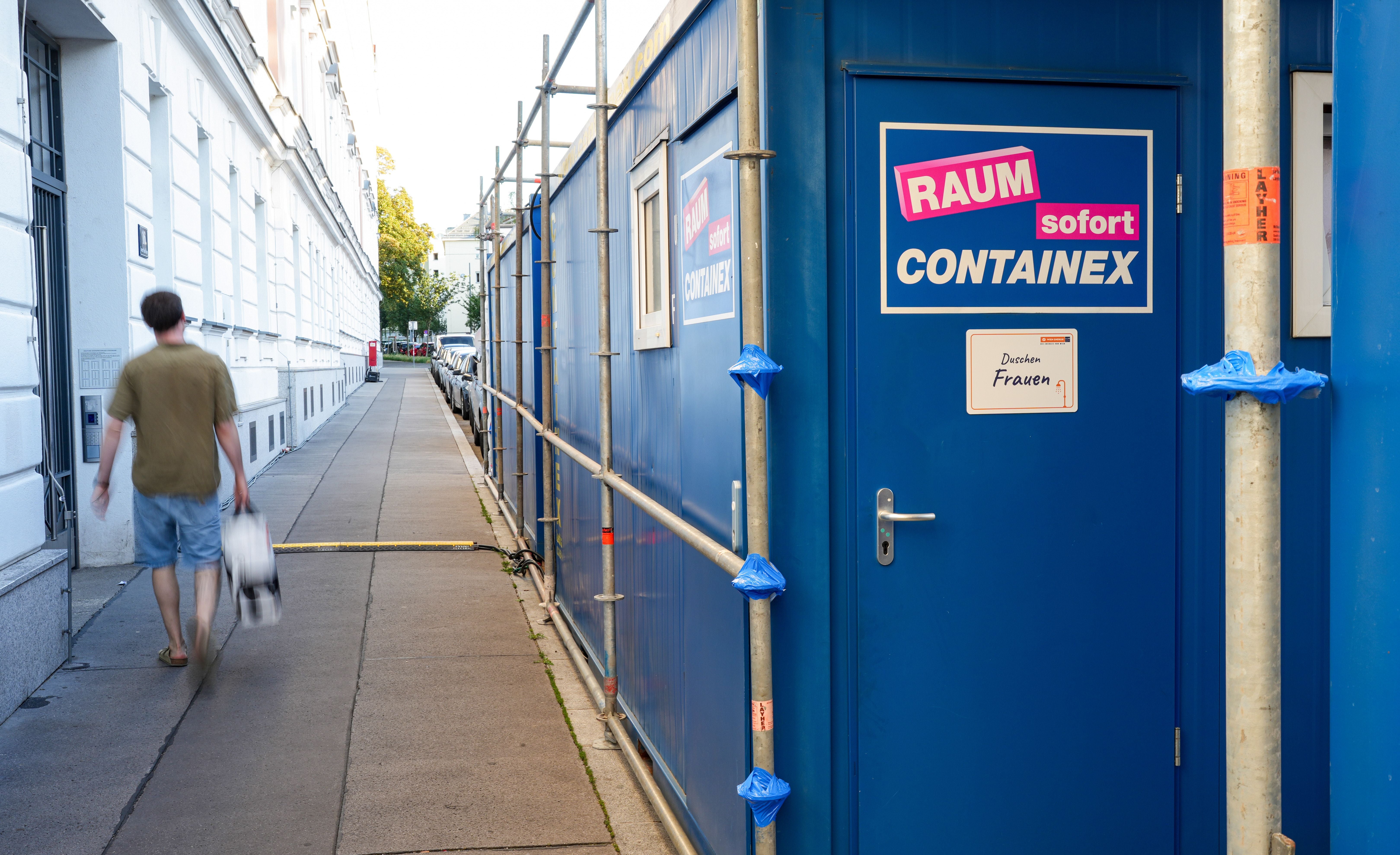 Blauer Duschcontainer für Frauen in der Lorenz-Mandl-Gasse, Wien, mit Mann auf dem Gehweg.