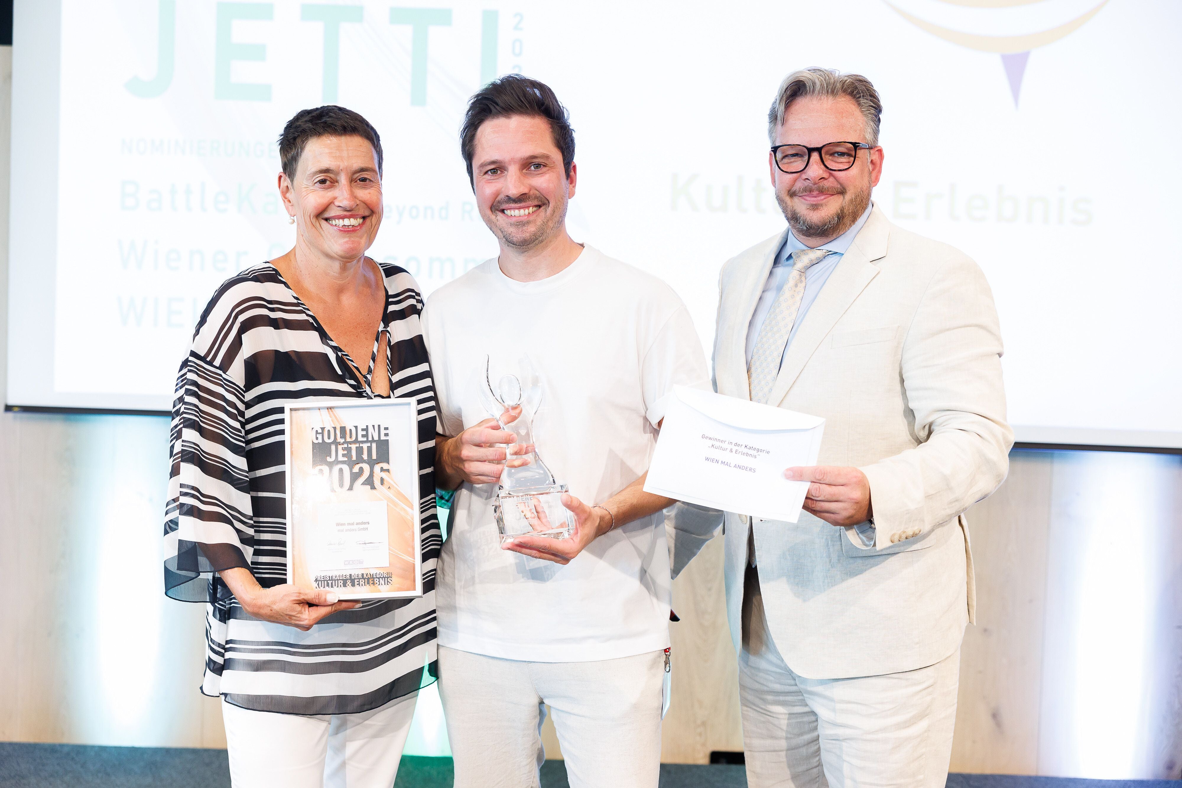 Drei Personen posieren bei einer Preisverleihung mit Urkunde, Pokal und Umschlag.