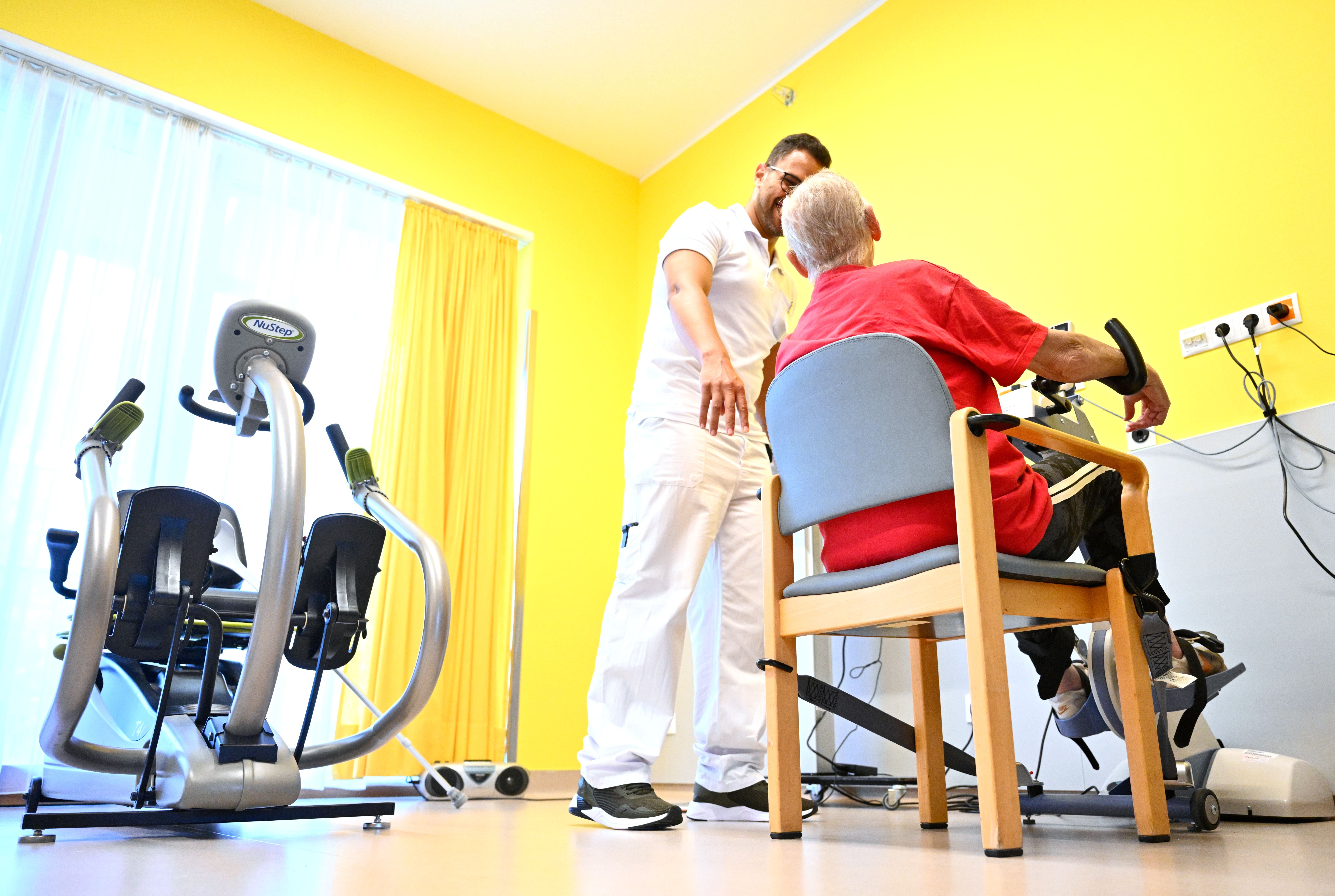 Eine Pflegekraft betreut eine ältere Person beim Training an einem Fitnessgerät in einem Pflegeheim.