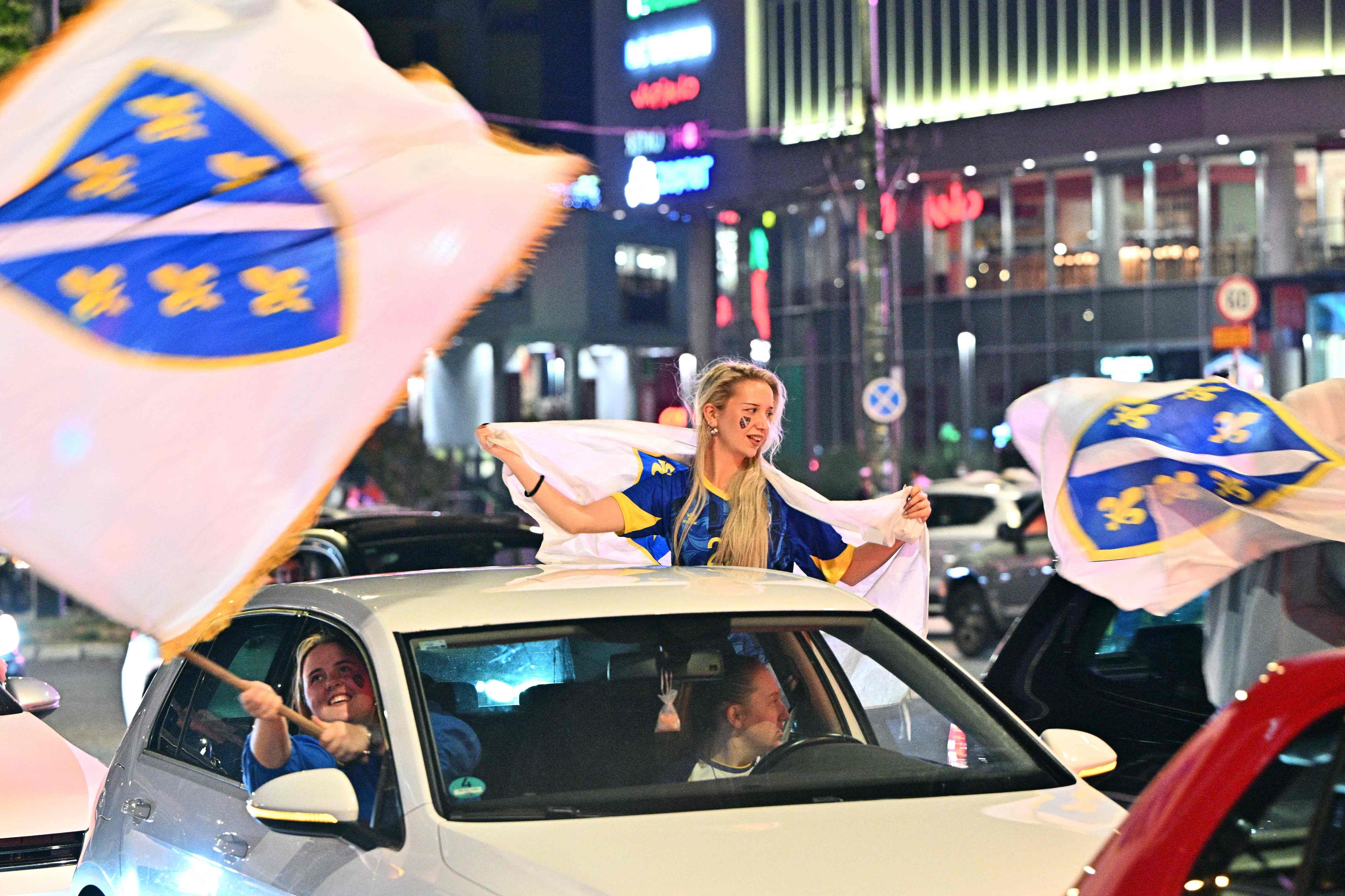 Fans feiern in Sarajevo mit bosnischen Flaggen durch Autofenster nach einem Fußballspiel bei Nacht.