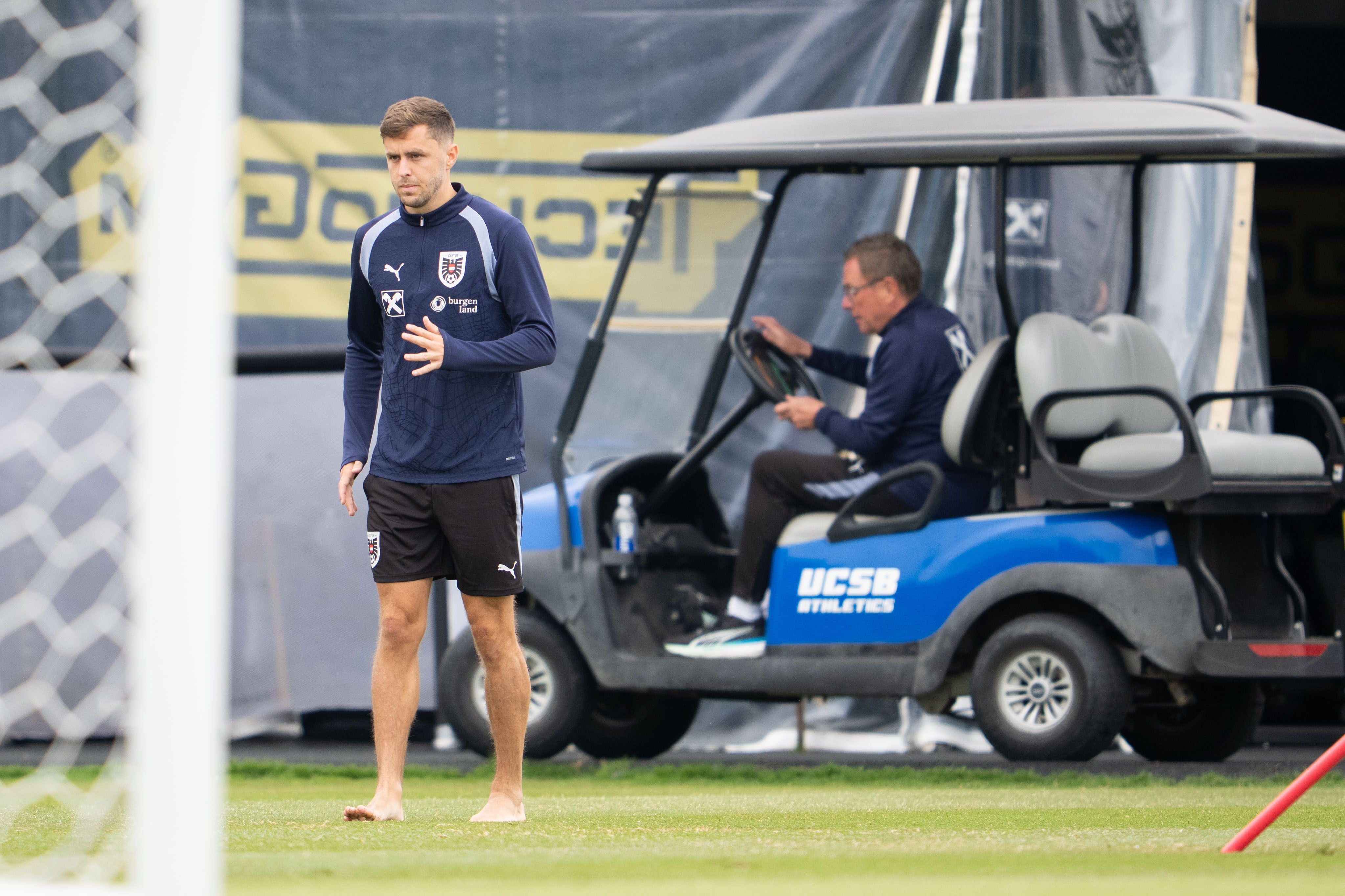 Christoph Baumgartner kommt barfuß aufs Trainingsfeld, im Hintergrund: Teamchef Ralf Rangnick im Golfcart.