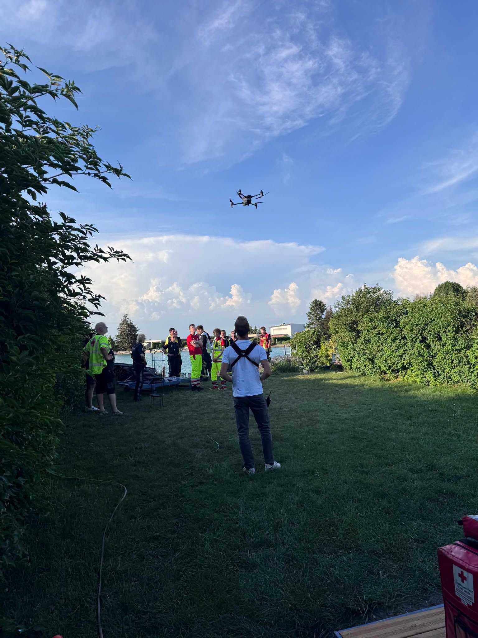 Menschen in Rettungswesten stehen auf einer Wiese, eine Drohne fliegt am Himmel.