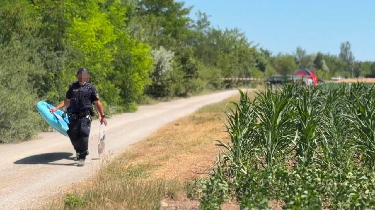 Ein Polizist trägt ein sichergestelltes SUP auf einem Feldweg neben einem Maisfeld.