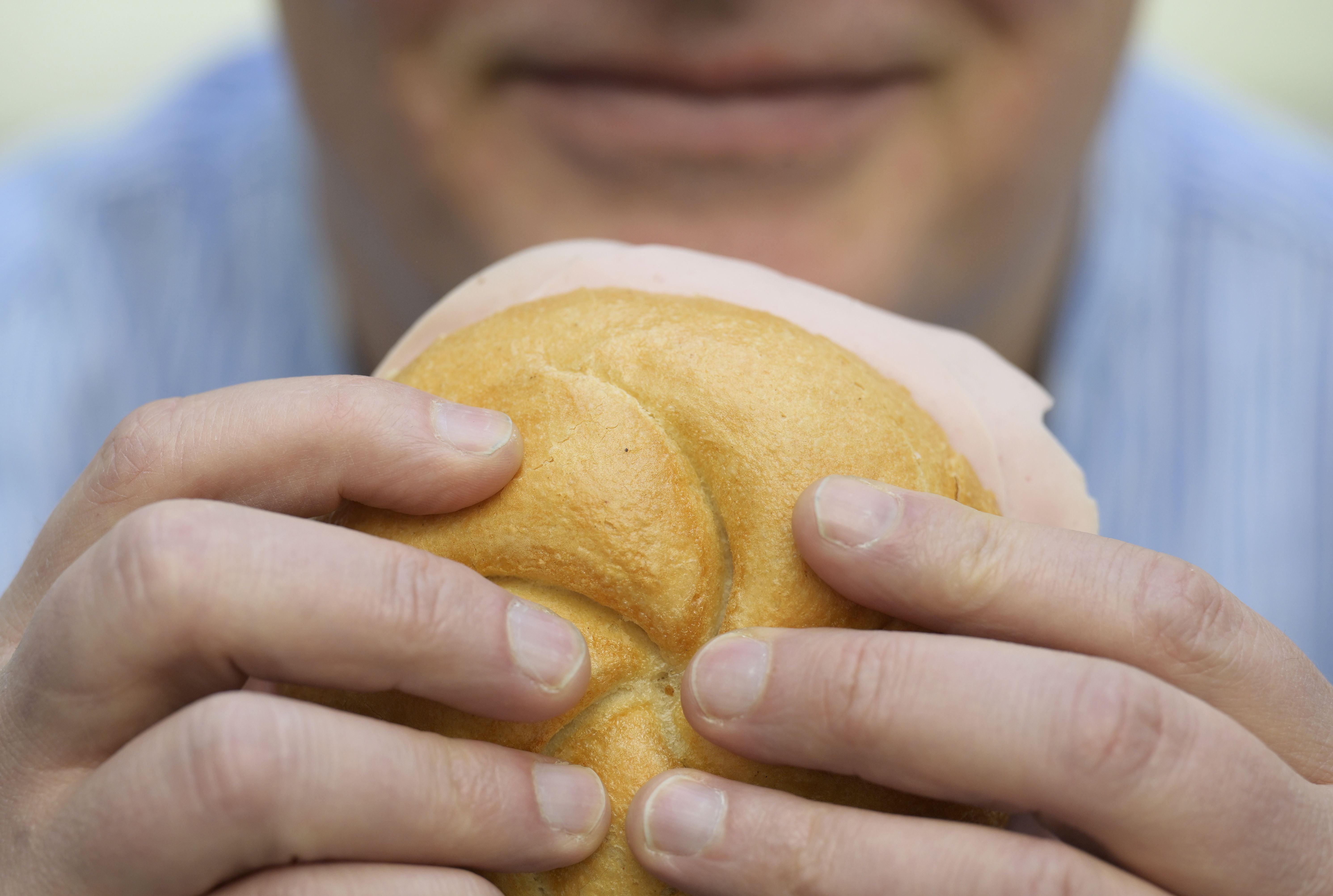 Ein Mann hält eine Wurstsemmel mit beiden Händen und will hineinbeißen.