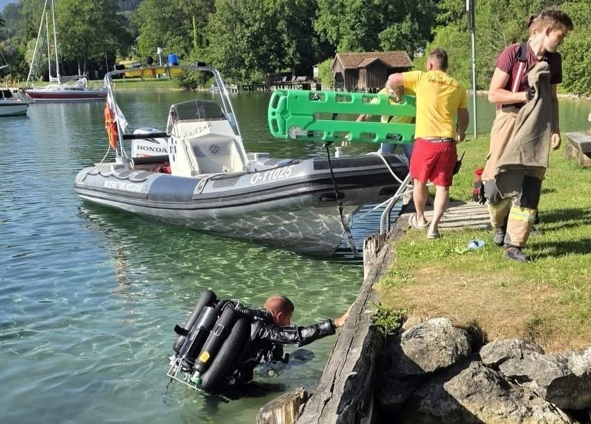 Taucher der Wasserrettung steigt am Ufer aus dem Wasser, zwei Helfer mit Rettungsbrett am Boot.