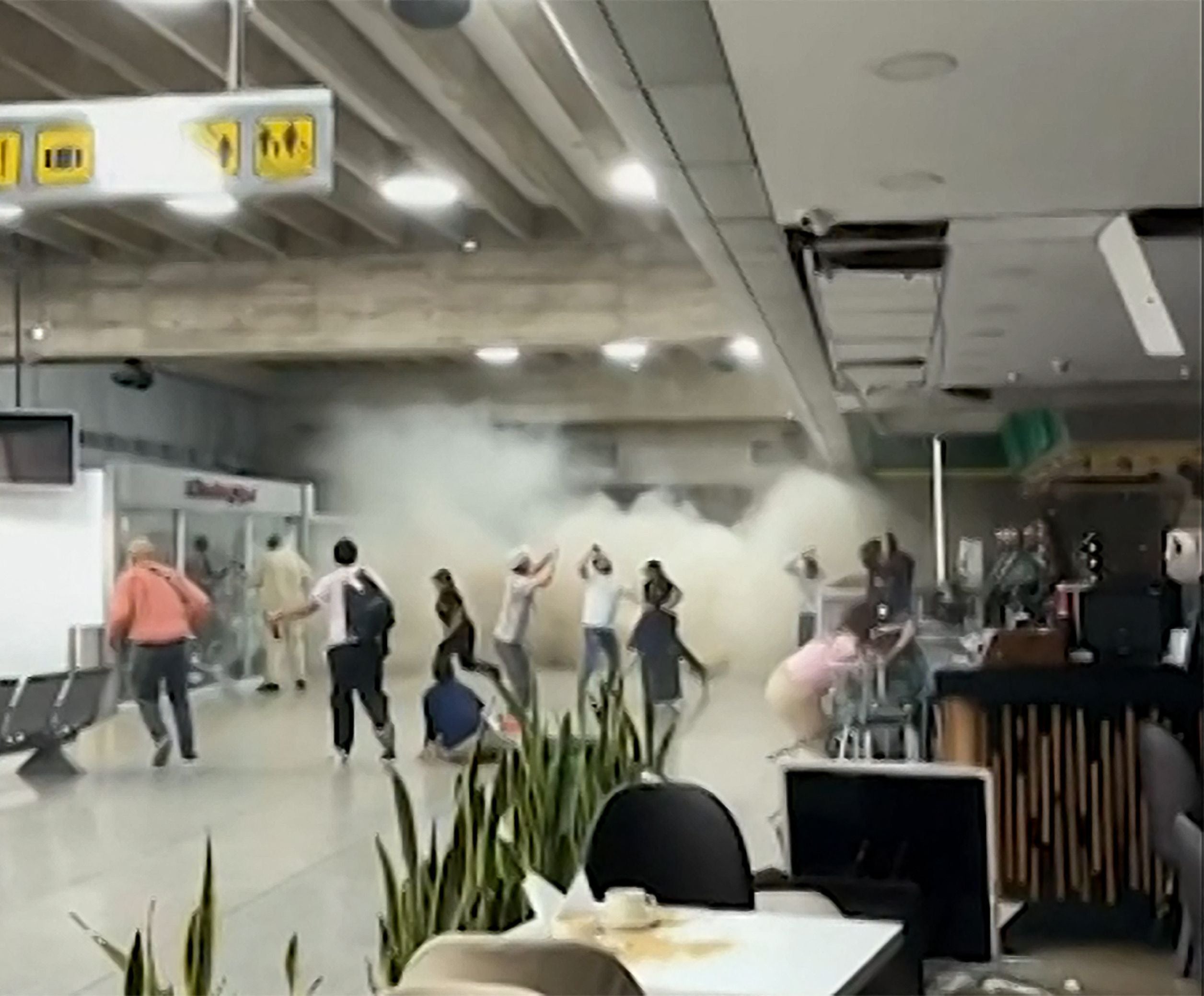 Menschen fliehen in einem Flughafen, während Staubwolken durch einen Teileinsturz aufwirbeln.
