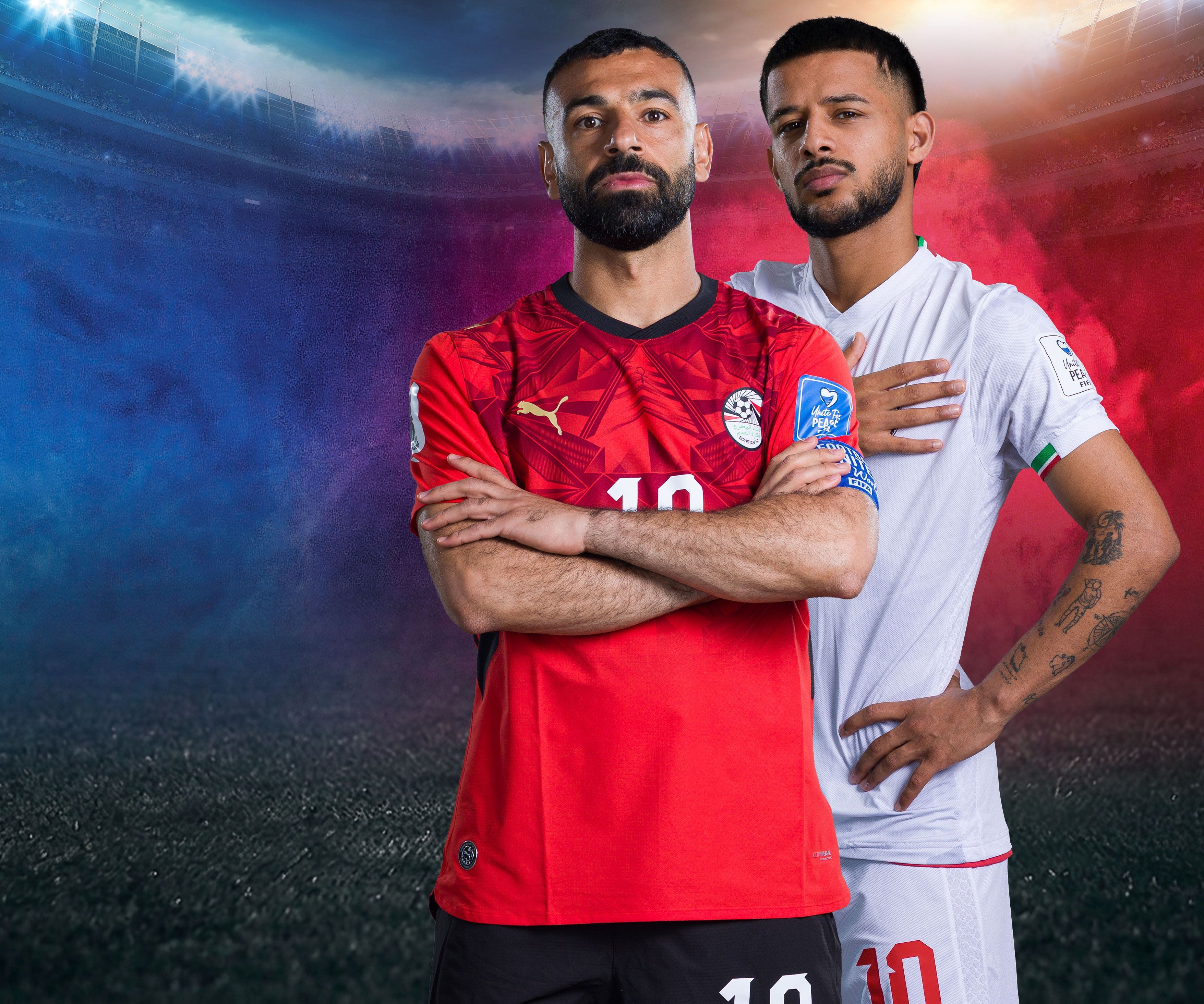 Zwei Fußballspieler aus Ägypten und Iran posieren im Stadion vor farbigem Hintergrund.