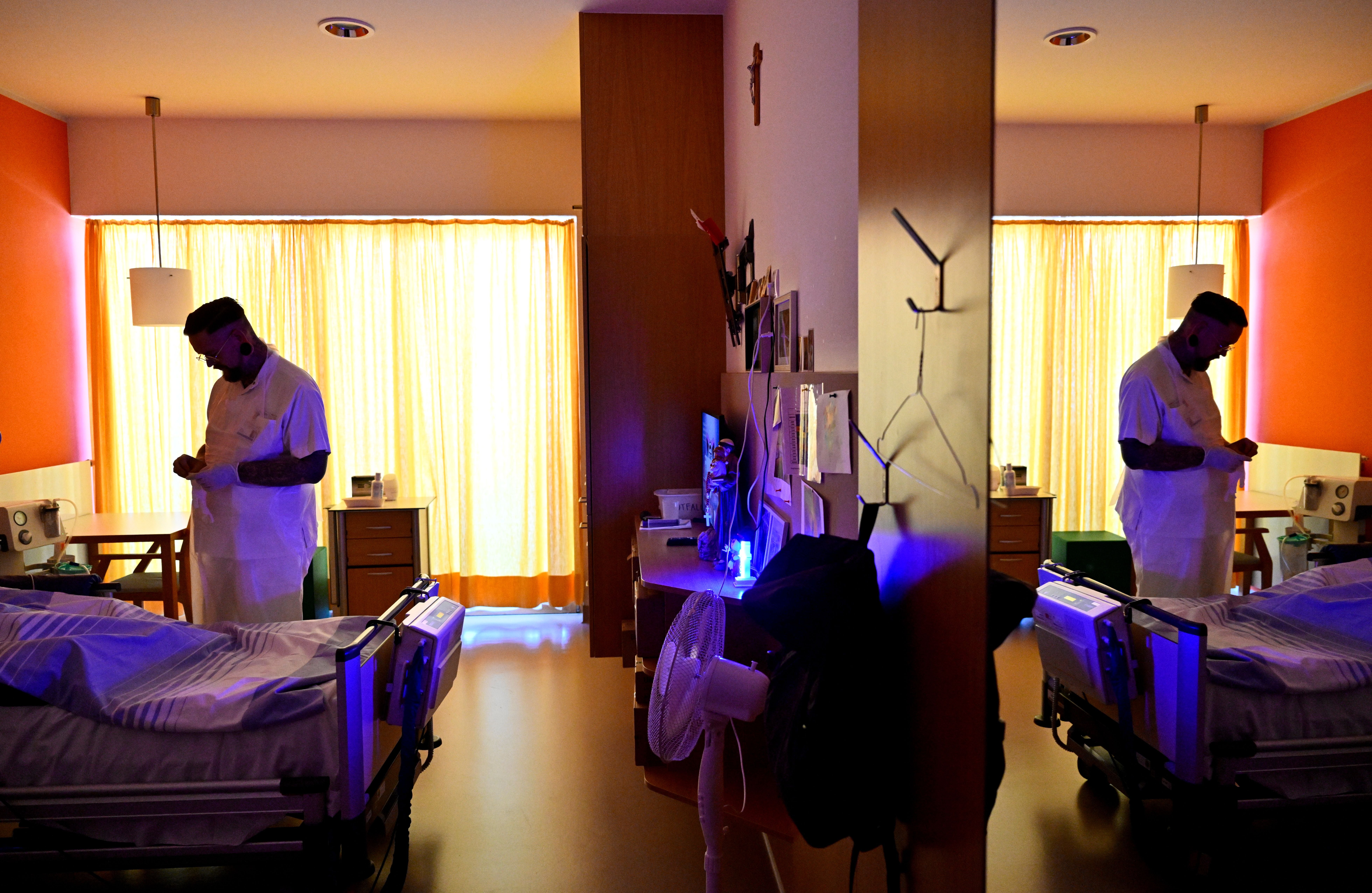 Pflegekraft steht am Bett eines Patienten in einem hell erleuchteten Pflegezimmer.